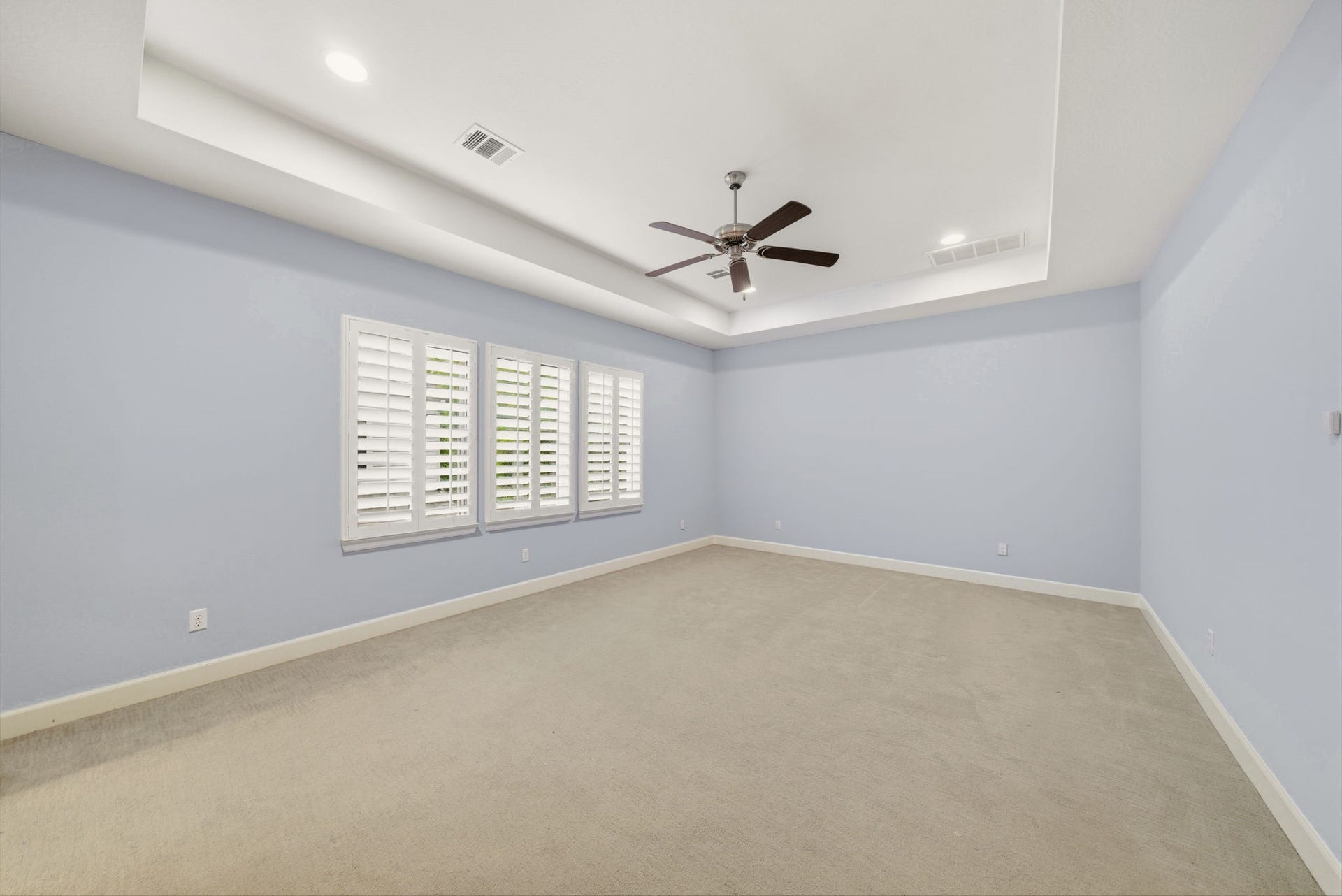 4926 Ella Boulevard, Houston, TX 77018 Spacious primary suite with tray ceiling, and a ceiling fan. The room features carpeted flooring, large windows with shutters, and an en-suite bathroom.