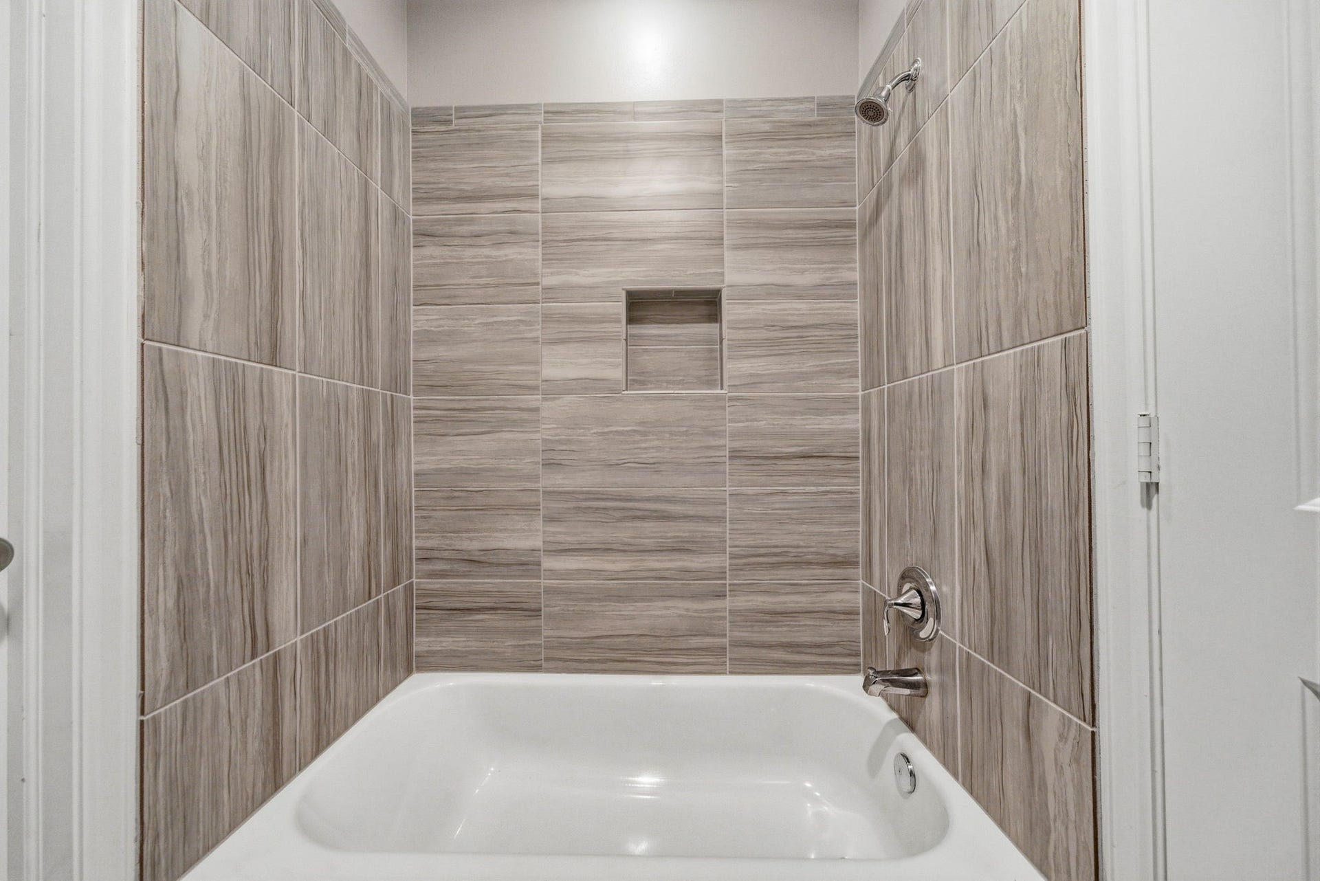 4926 Ella Boulevard, Houston, TX 77018 Guest bathroom features a modern bathtub with elegant wood-look tile walls and a convenient built-in niche for storage.