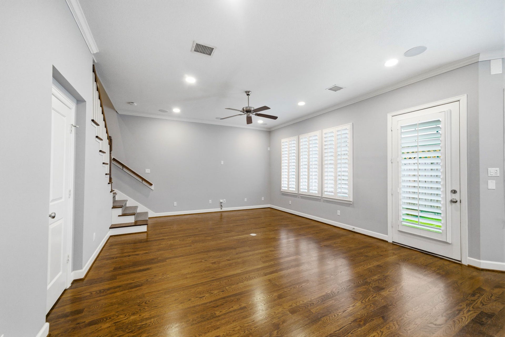 4926 Ella Boulevard, Houston, TX 77018 Spacious living area with hardwood floors, neutral walls, and recessed lighting. Features large windows with plantation shutters, a ceiling fan, and a door leading outside to the rear yard that has beautiful turf.