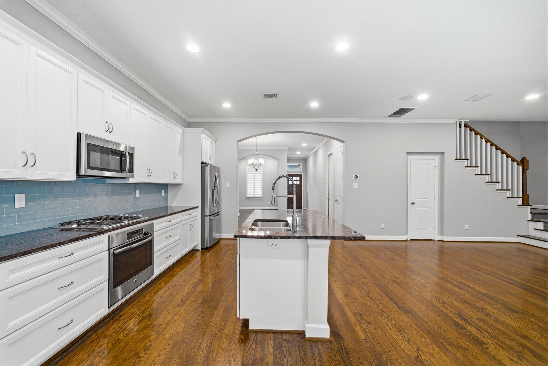 4926 Ella Boulevard, Houston, TX 77018 Spacious open-concept island kitchen and living area with hardwood floors. The kitchen features white cabinets, stainless steel appliances, and a central island with a sink. The area is well-lit with natural light.