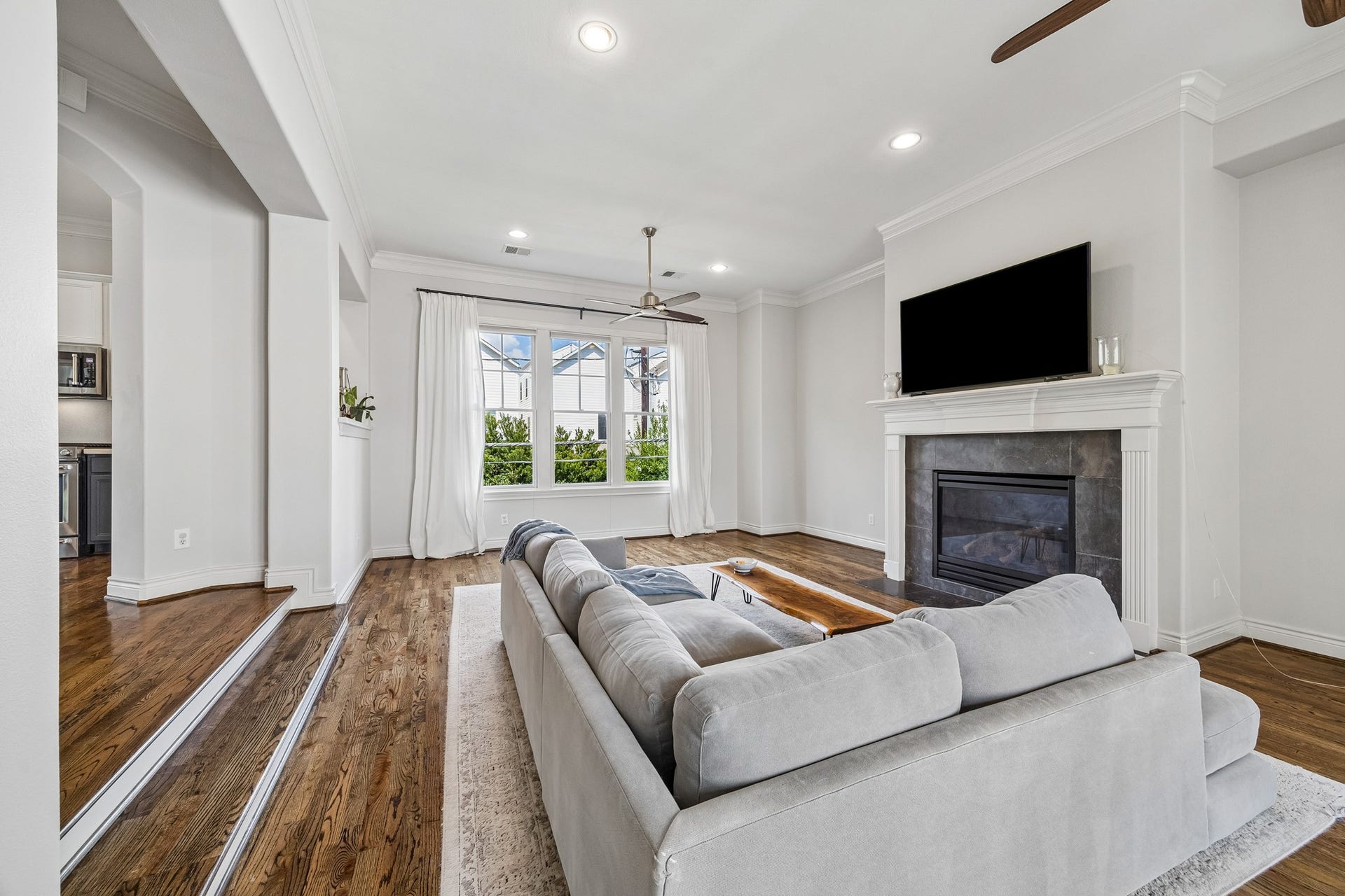 Spacious 2nd floor  living room featuring solid oak hardwood floors, a cozy fireplace, and large windows that fill the space with natural light. Note the crown molding and upgraded ceiling fans.