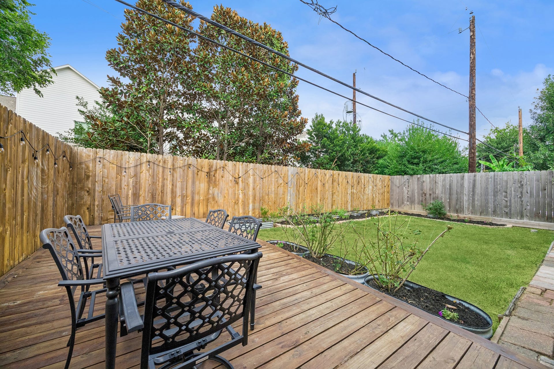 Charming and very private backyard retreat with a spacious wooden deck perfect for outdoor dining, surrounded by landscaping and lawn.