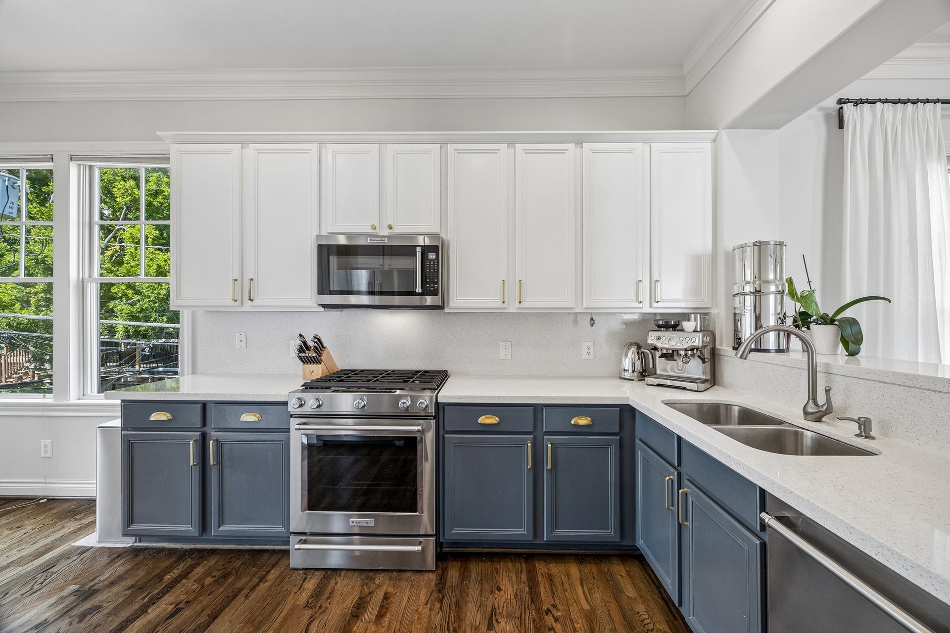 The updated kitchen (2021) with elegant two-tone cabinetry, brushed gold hardware, and sleek quartz countertops, enhanced by natural light from large windows provides an open concept for entertaining with just enough separation.