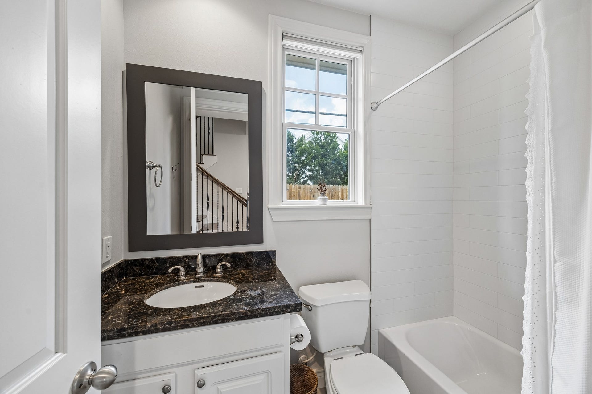 First floor hallway bath featuring a sleek granite countertop, modern fixtures, and a tub/shower combo , a bright window fills the space with natural light.