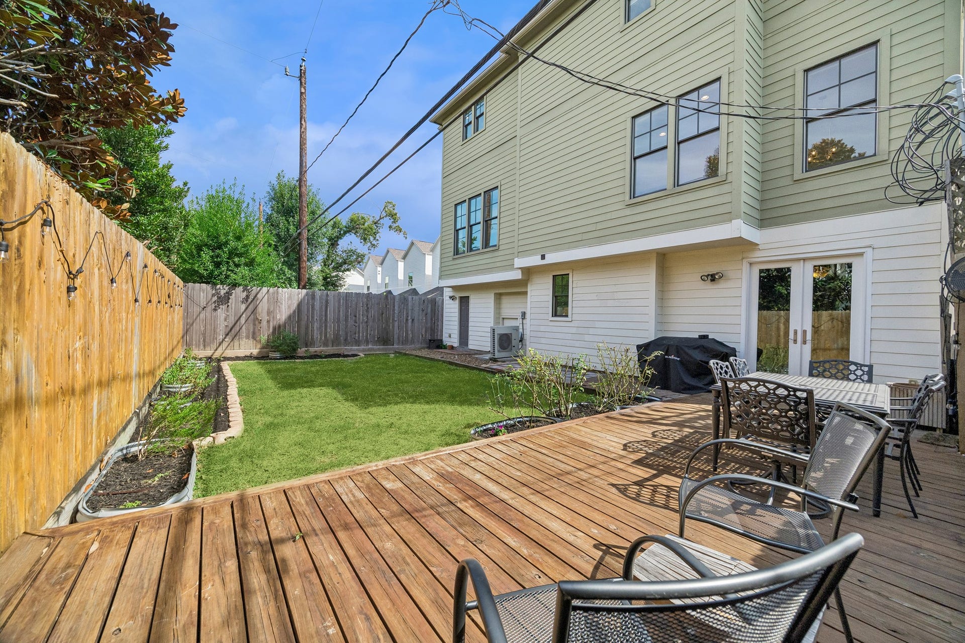 Welcoming backyard retreat featuring a large wooden deck for outdoor dining, green lawn, and privacy fencing, perfect for relaxation and entertaining.