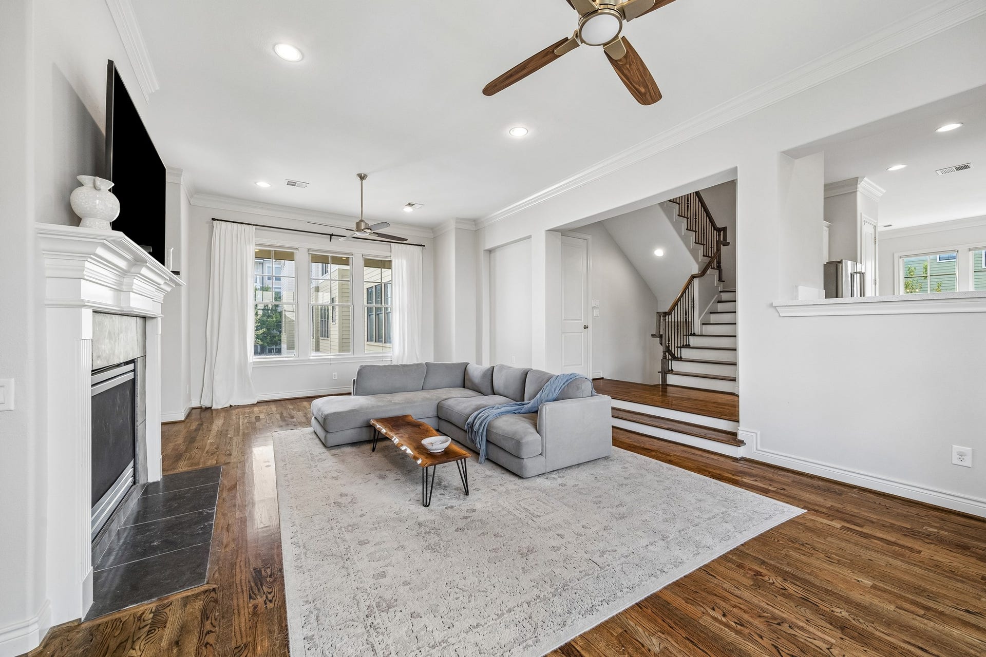 Another view of the 2nd floor living room seamlessly connected to the kitchen to the right , powder room and stairs leading up to the other floors. Crown molding and updated fans polish off the finishes.