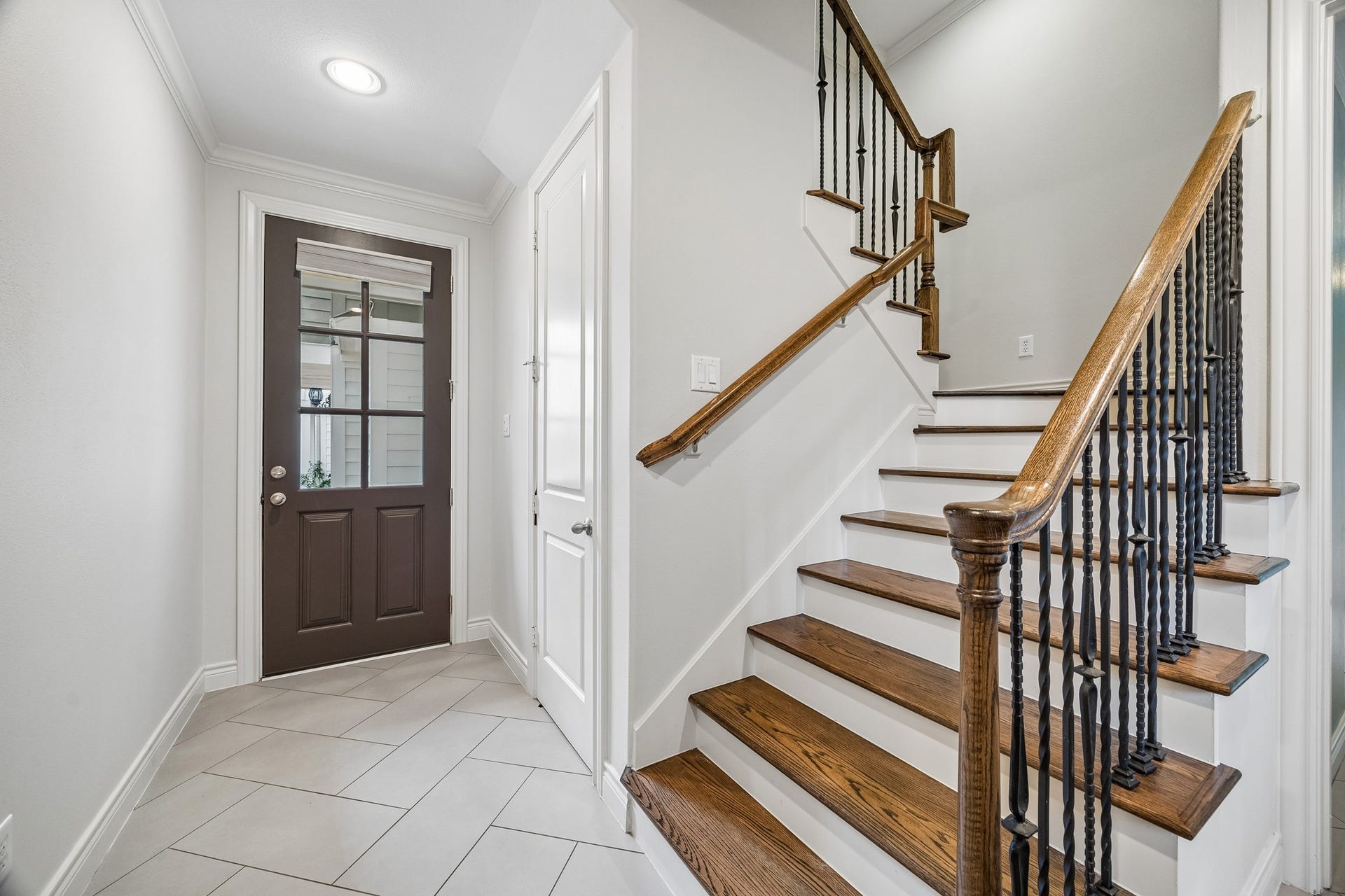 Elegant entryway features a classic wooden staircase with wrought iron railings and complemented by a herringbone patterned tile floor. The glass panels in the front door let in tons of natural light creating a welcoming entryway. Crown molding adds a refined finish here and throughout the home.