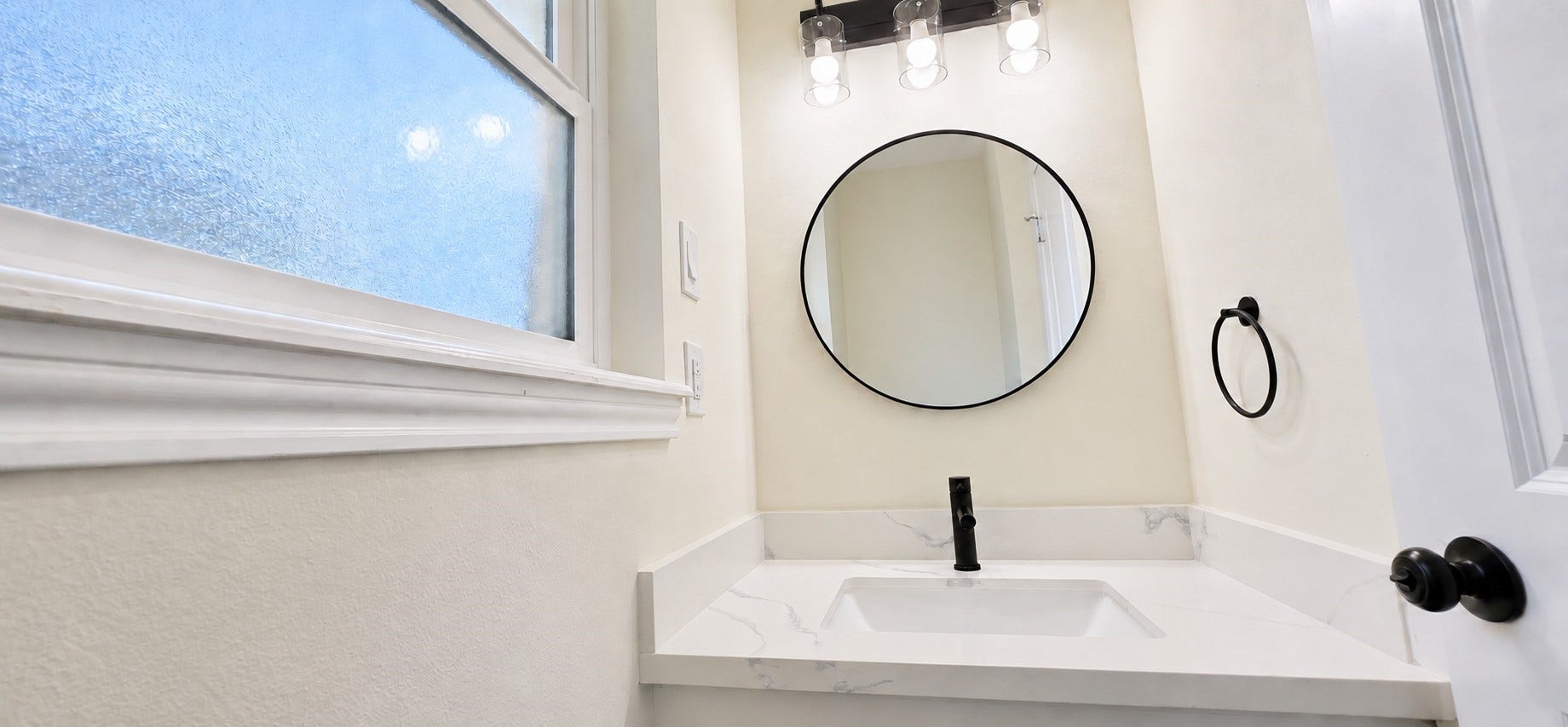 5527 Wigton Drive, Houston, TX 77096 Stylish powder room features a veined countertop, matte-black faucet, round mirror, and frosted window.