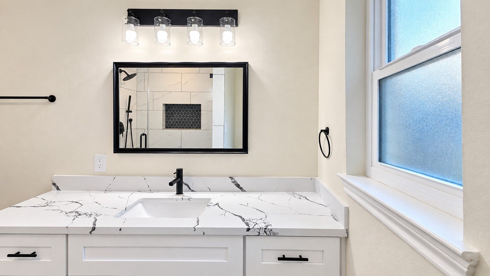 5527 Wigton Drive, Houston, TX 77096 Updated primary bath vanity pairs veined countertops, matte-black fixtures, and natural light from the frosted window.