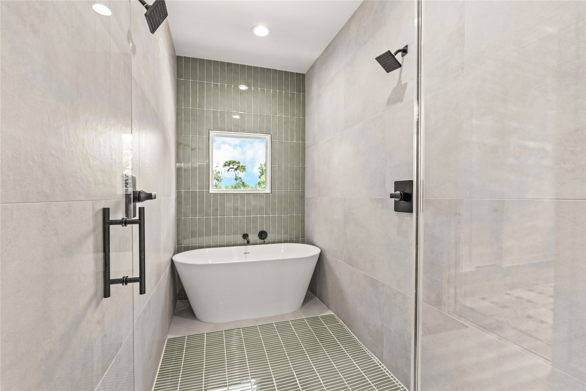 7432-7444 Tremper Street, Houston, TX 77020 Inside view of the primary wet room/shower area featuring full wall tiling, a freestanding soaking tub nestled under a window, and a green-tiled accent floor.