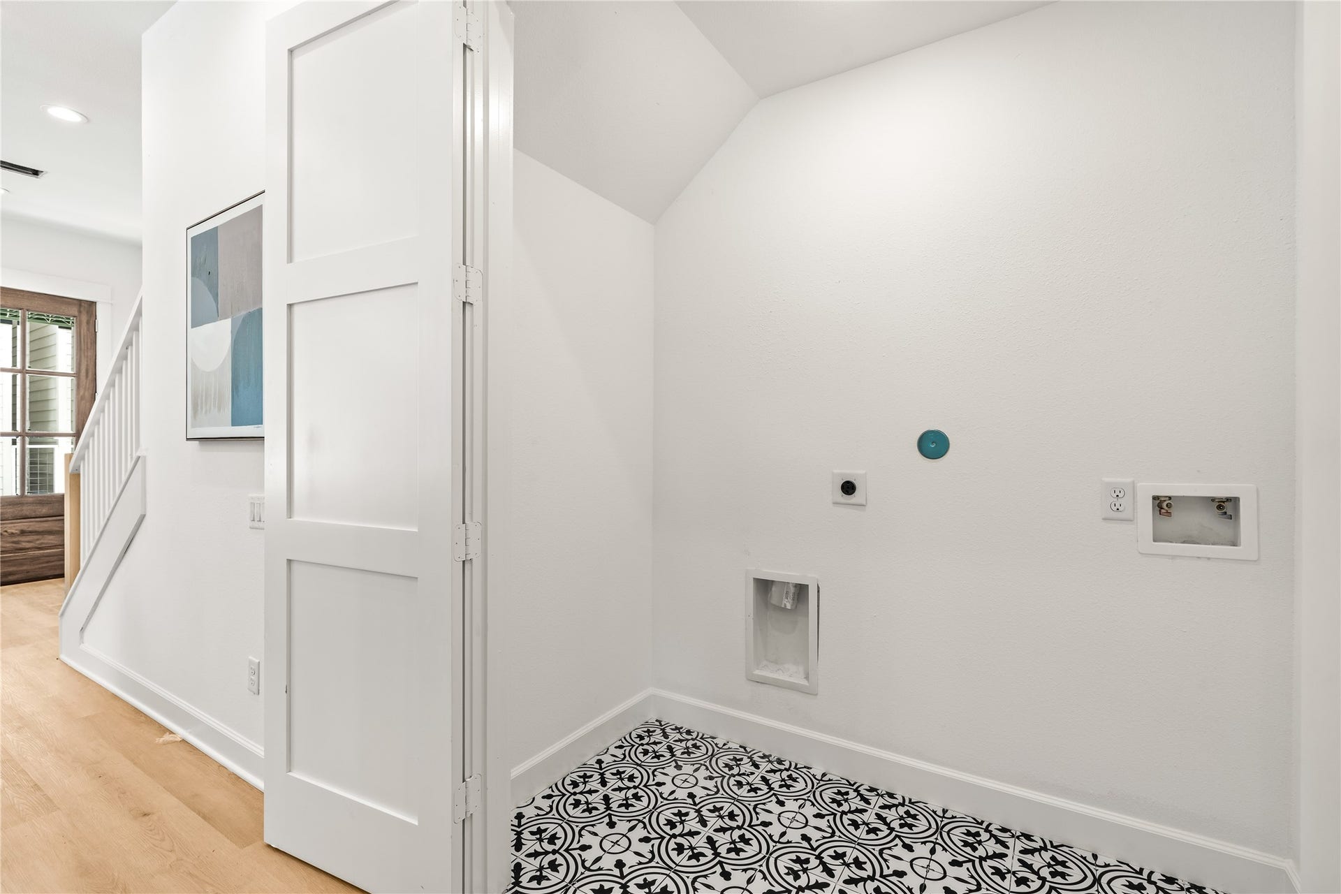 7432-7444 Tremper Street, Houston, TX 77020 A dedicated laundry closet nestled under the stairs, showcasing graphic black-and-white patterned floor tile, standard utility hookups, and a white bifold privacy door.