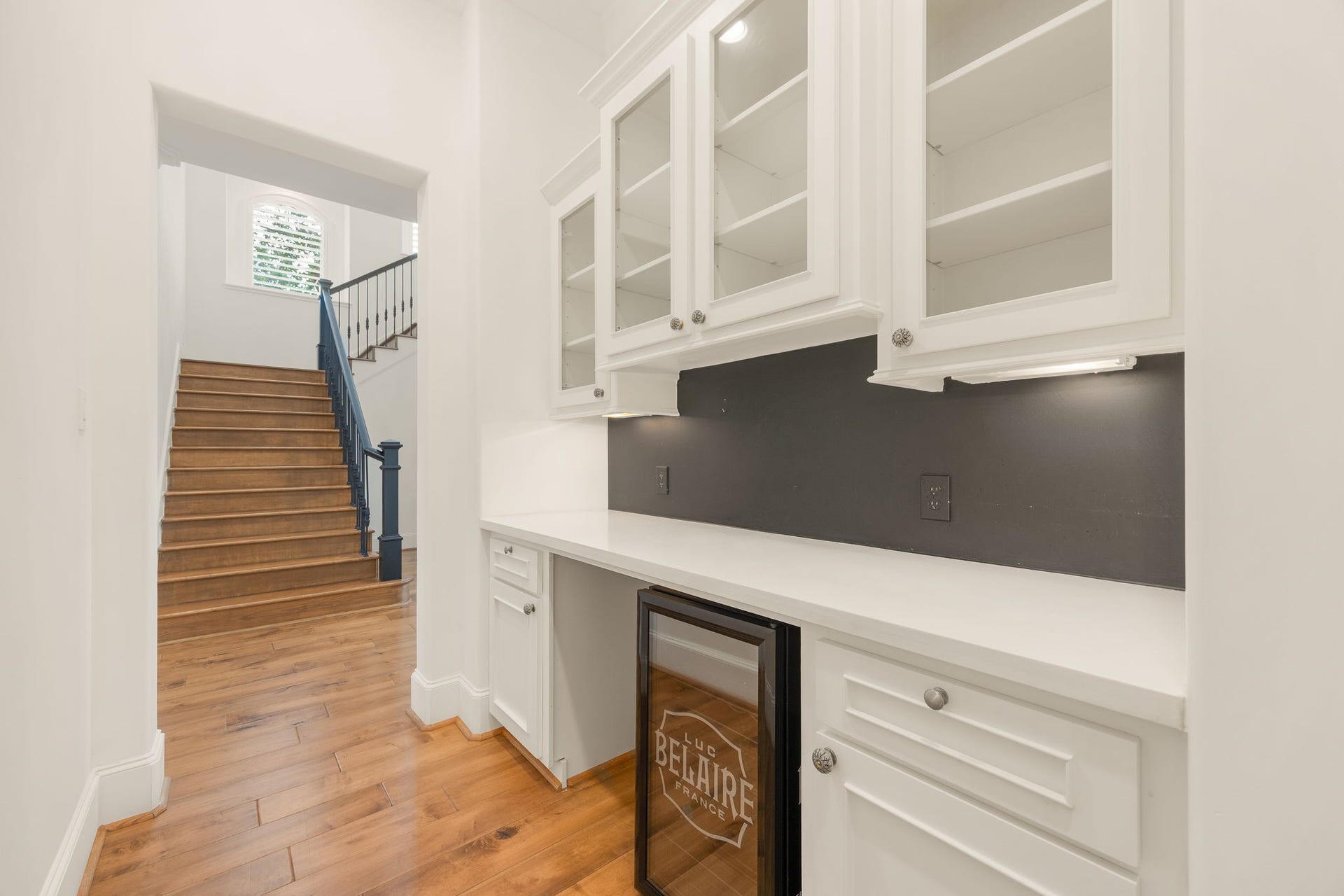 Hosting just got easier with this beautifully appointed butlers pantry, featuring crisp white cabinetry, glass front upper cabinets, generous counter space, and a built in beverage refrigerator! Perfect for keeping drinks chilled and serving essentials close at hand, this thoughtful space adds a touch of luxury to every gathering.