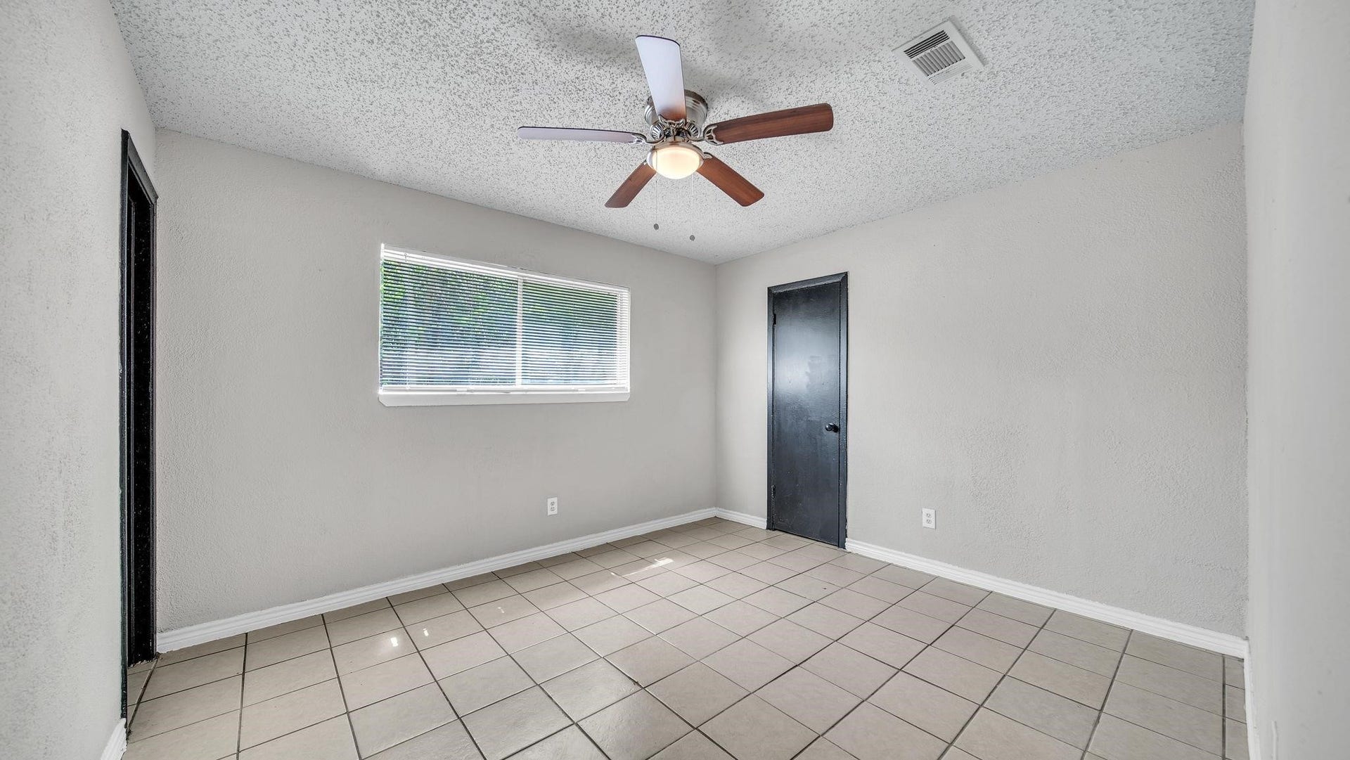 10902 Jutland Road, Houston, TX 77048 This inviting secondary bedroom features tile flooring, a ceiling fan with integrated lighting, and a spacious walk-in closet. A sliding window overlooks the backyard, welcoming natural light and offering a pleasant view of the outdoor surroundings.