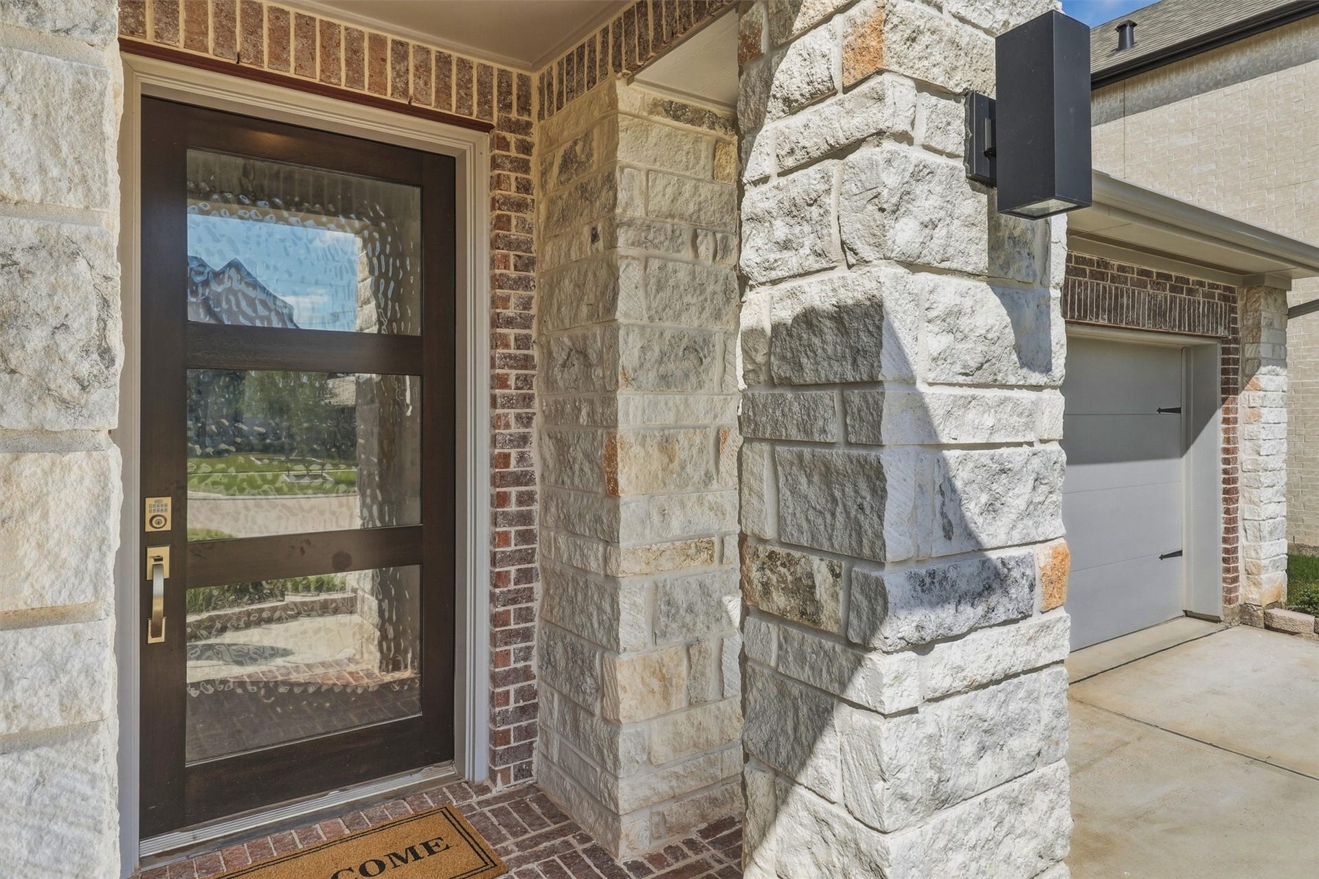 30135 Gold Finch Place, Fulshear, TX 77441 The inviting front entry showcases impressive stone and brick craftsmanship, sleek contemporary lighting, and an upgraded front door with decorative privacy glass and keyless entry. Clean architectural lines and quality finishes create a warm, welcoming arrival for family and guests alike.