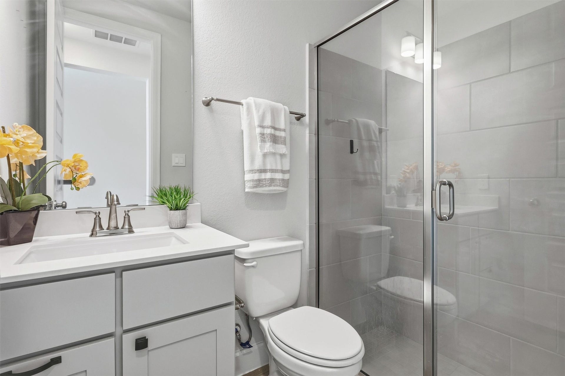 30135 Gold Finch Place, Fulshear, TX 77441 A beautifully appointed secondary bathroom features a sleek quartz vanity, shaker-style cabinetry, designer lighting, and a spacious glass-enclosed walk-in shower with oversized tile, offering guests and family a stylish, comfortable retreat.