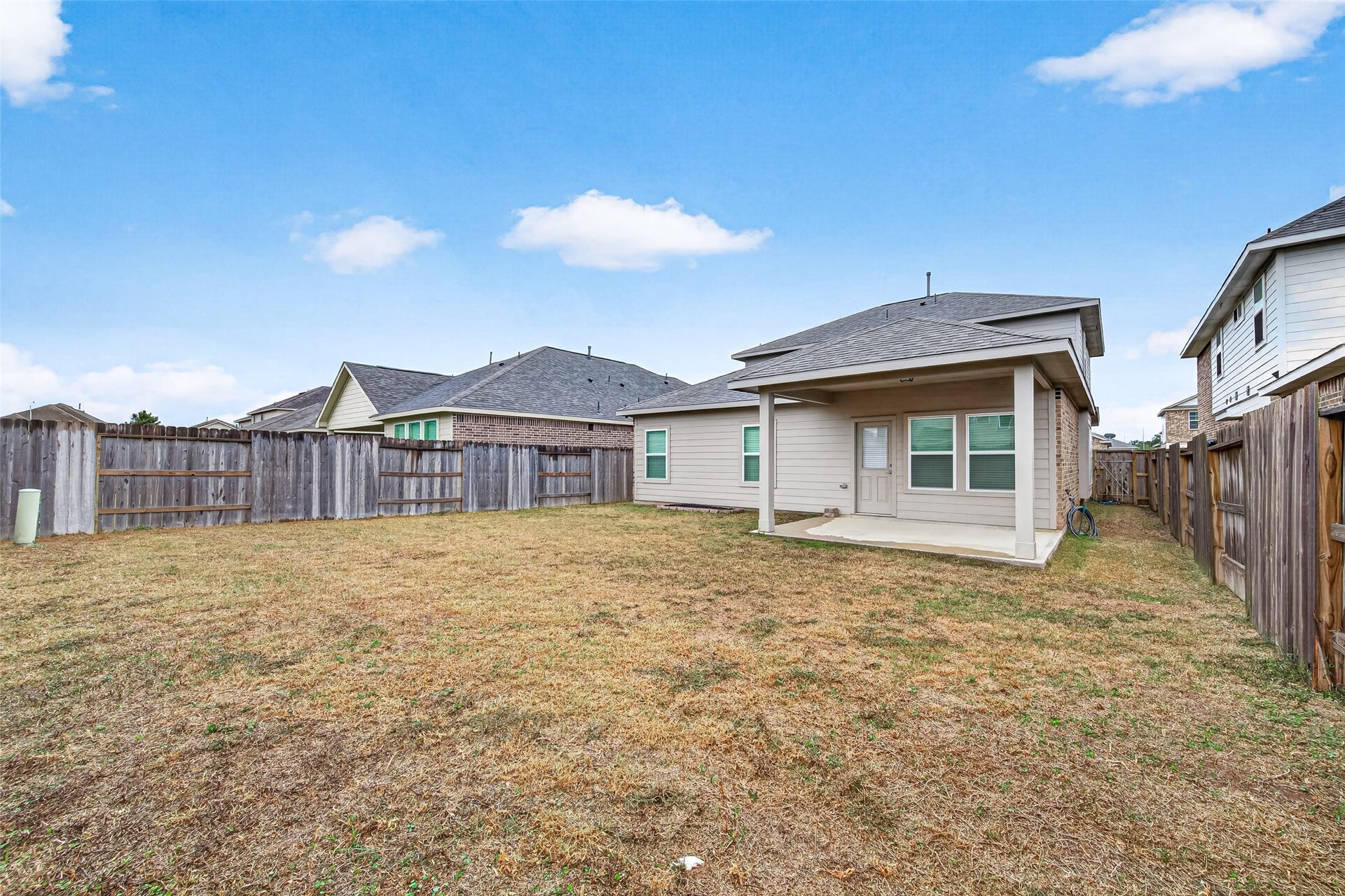 32922 Ruthie Dean Drive, Fulshear, TX 77423 A view across the fenced backyard showcases the rear exterior and covered patio, with open lawn space to enjoy.
