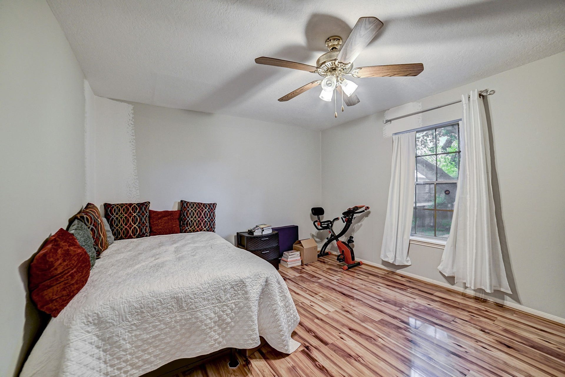 7900 Westheimer Road, #202, Houston, TX 77063 Cozy bedroom with warm wooden flooring, a ceiling fan, and ample natural light streaming through the large window.
