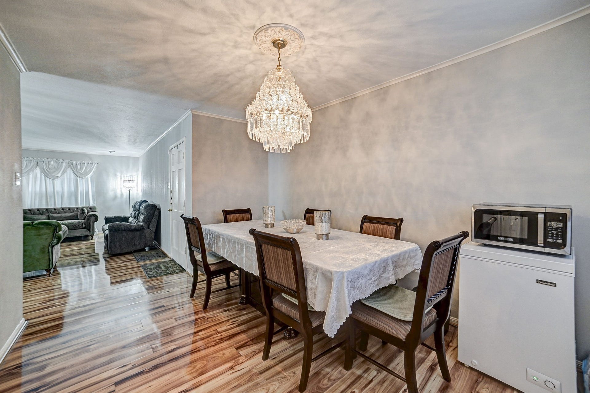 7900 Westheimer Road, #202, Houston, TX 77063 Elegant dining area with a stunning chandelier and rich wood flooring, seamlessly connected to a cozy living space filled with natural light.