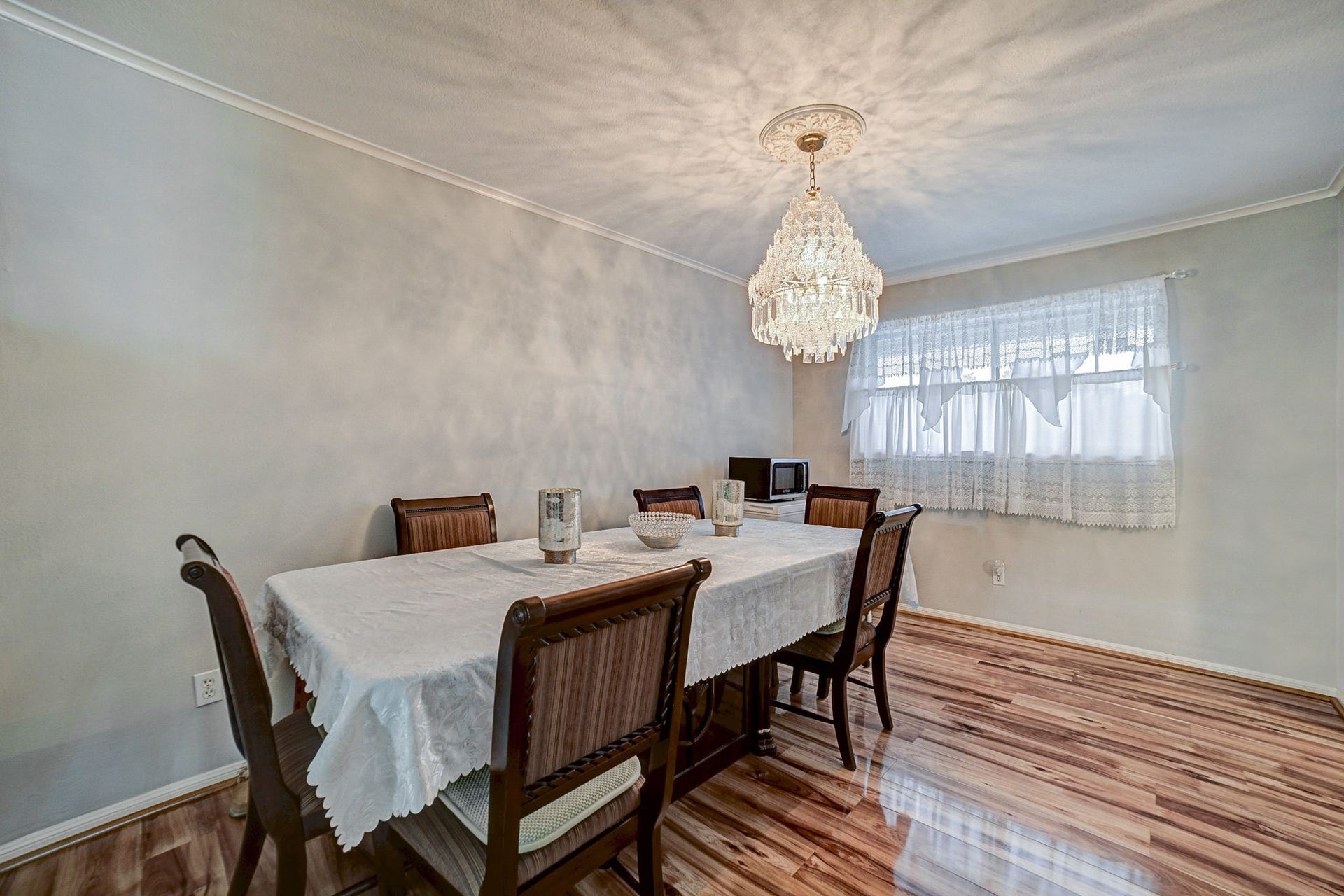 7900 Westheimer Road, #202, Houston, TX 77063 Elegant dining room featuring a stunning chandelier, polished wood flooring, and a large window with lace curtains, creating a bright and inviting space for gatherings.