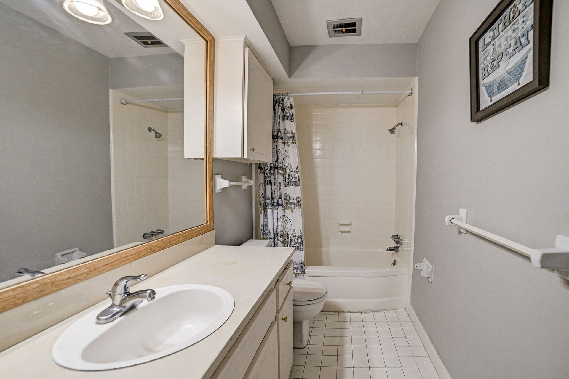 7900 Westheimer Road, #202, Houston, TX 77063 Charming bathroom with a large mirror, sleek countertop, and a shower-tub combo featuring a decorative curtain. Neutral tones create a calming atmosphere.