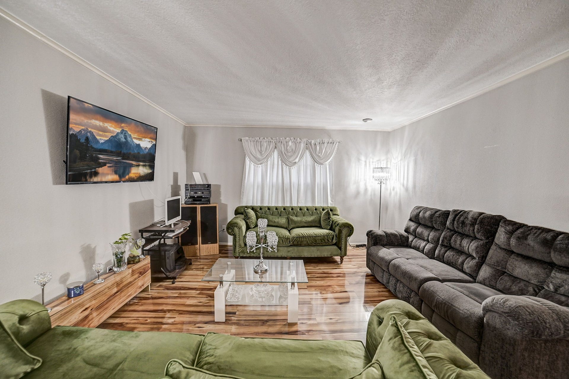 7900 Westheimer Road, #202, Houston, TX 77063 Spacious living room with elegant wood flooring, featuring plush green and gray seating, a wall-mounted TV, and ample natural light from a large window.