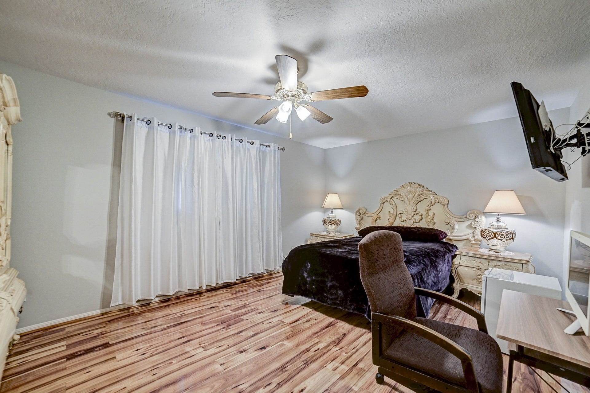 7900 Westheimer Road, #202, Houston, TX 77063 Elegant bedroom features rich wood flooring, a luxurious carved headboard, and soft ambient lighting from stylish bedside lamps.