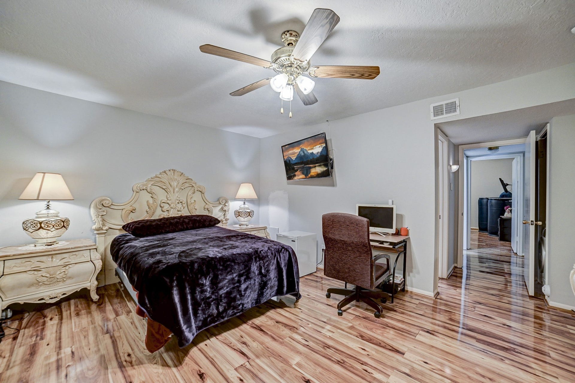 7900 Westheimer Road, #202, Houston, TX 77063 Charming bedroom with elegant carved furniture, warm wood flooring, and a cozy workspace, all illuminated by soft lighting and a ceiling fan.