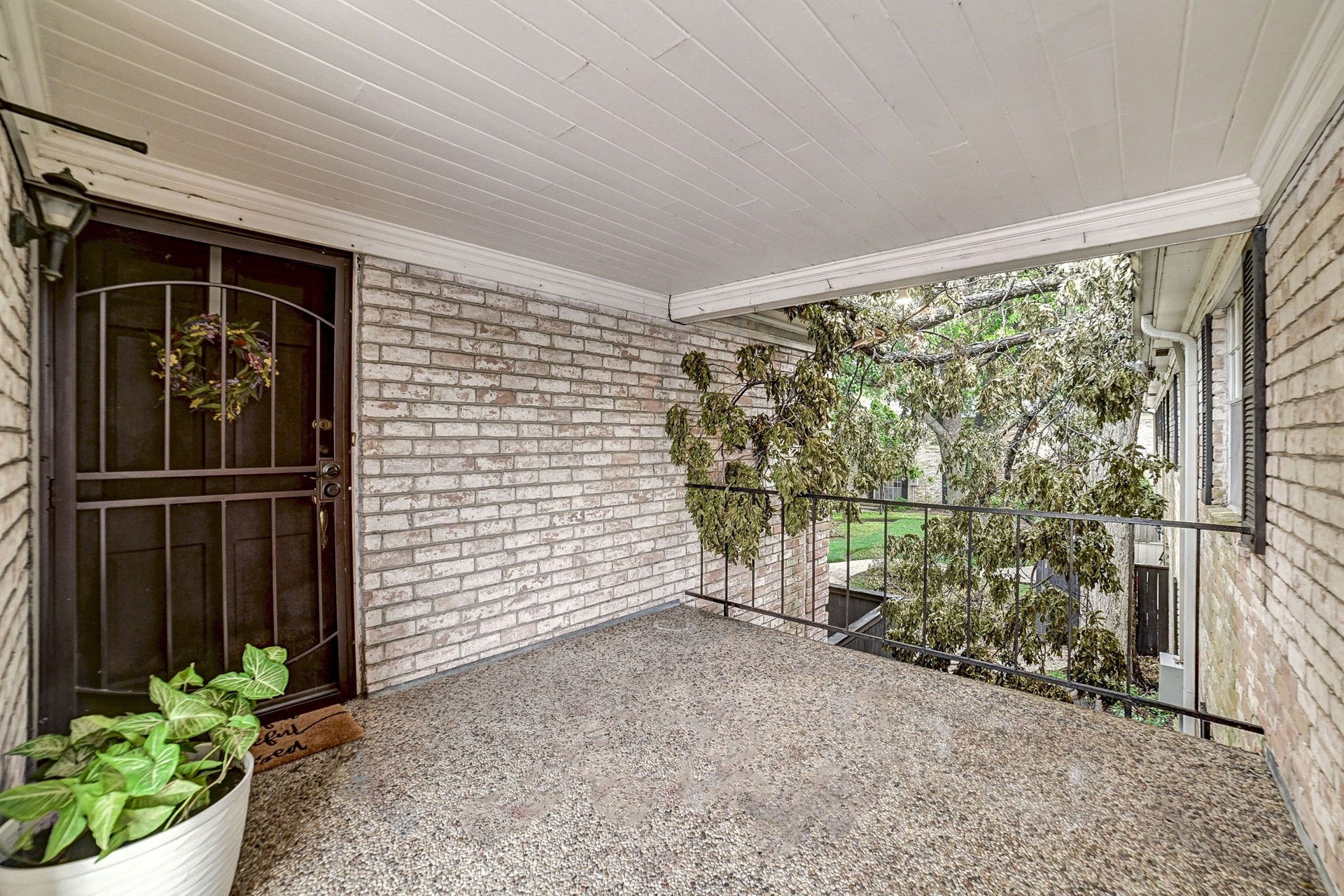 7900 Westheimer Road, #202, Houston, TX 77063 Charming covered porch with a brick facade and wrought iron door, perfect for enjoying the outdoors.
