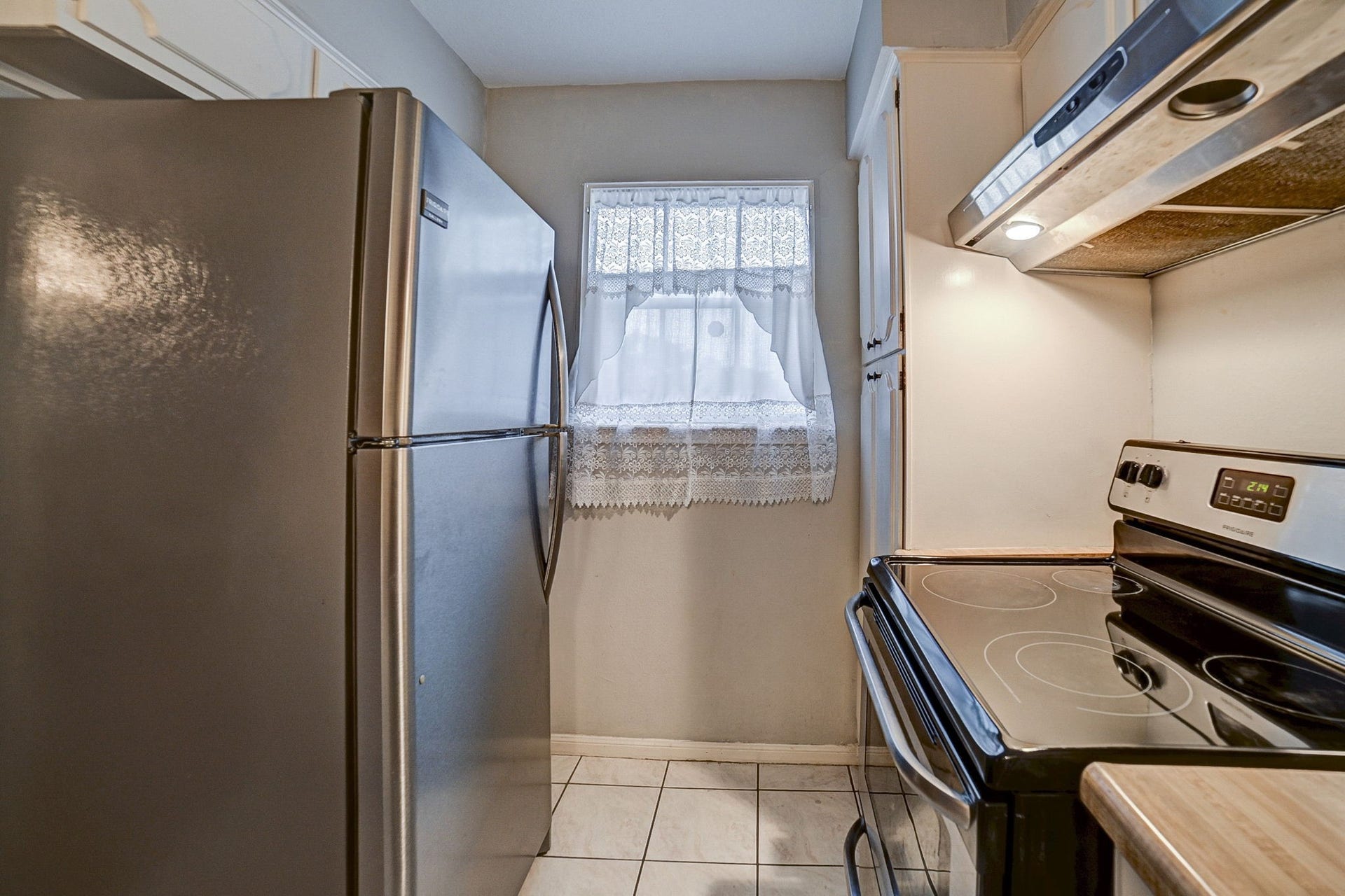 7900 Westheimer Road, #202, Houston, TX 77063 Cozy kitchen featuring a sleek stainless steel refrigerator and modern electric stove, complemented by a charming window with lace curtains for natural light.