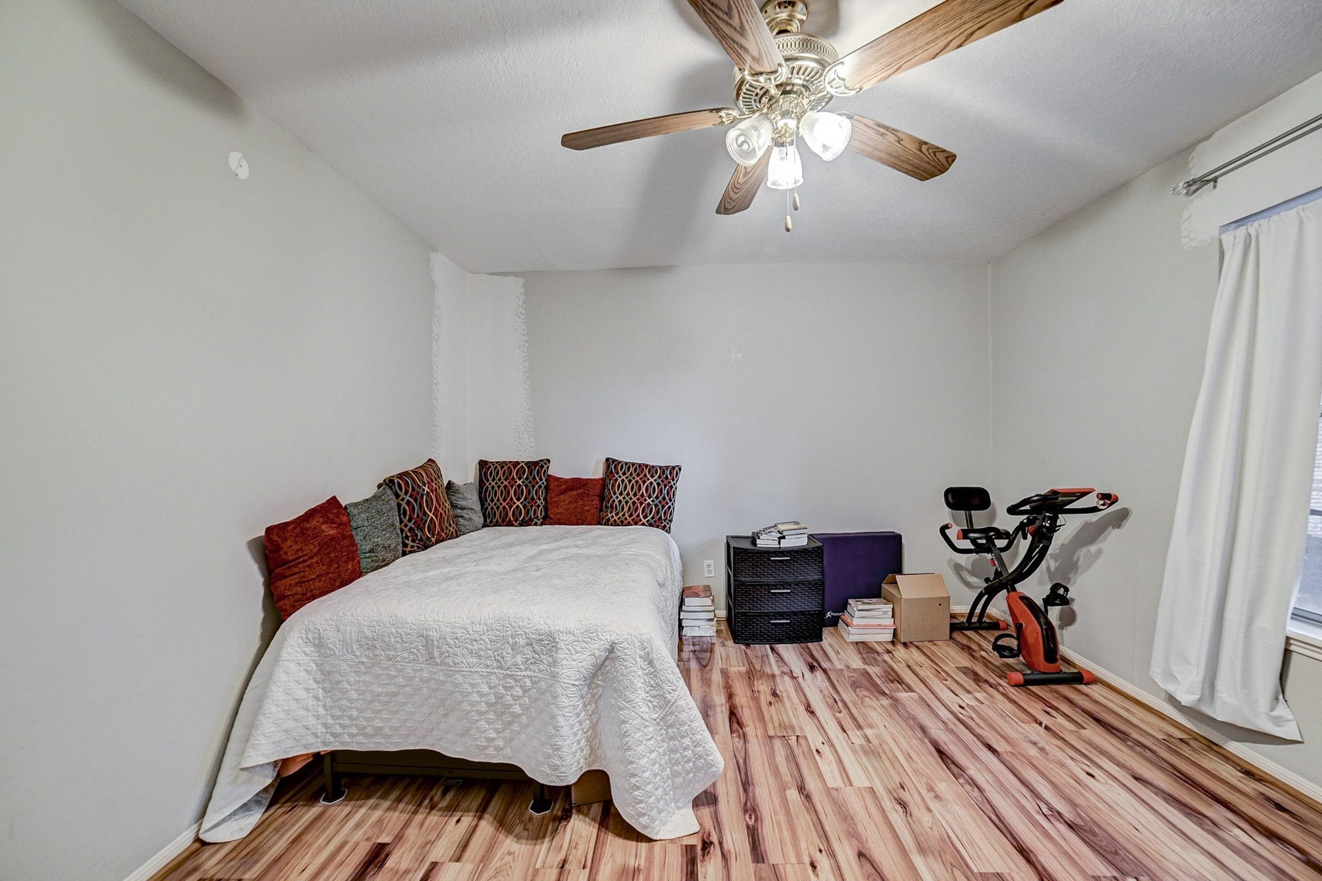 7900 Westheimer Road, #202, Houston, TX 77063 Cozy bedroom with warm wood flooring, ceiling fan, and plenty of natural light, perfect for relaxation or a home gym setup.