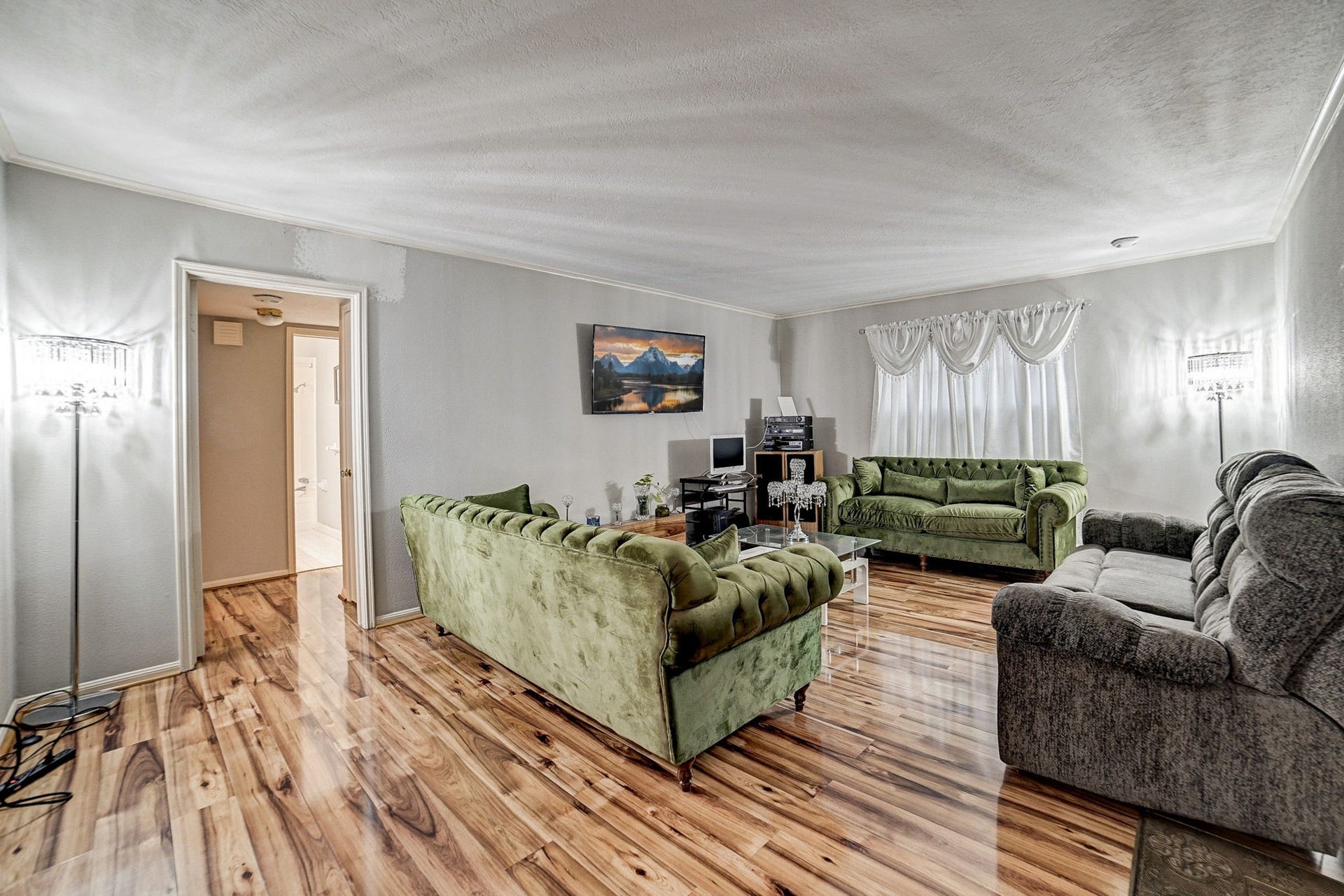 7900 Westheimer Road, #202, Houston, TX 77063 Spacious living room with elegant wood flooring, featuring plush green and gray sofas, ambient lighting, and a cozy atmosphere perfect for relaxation and entertainment.