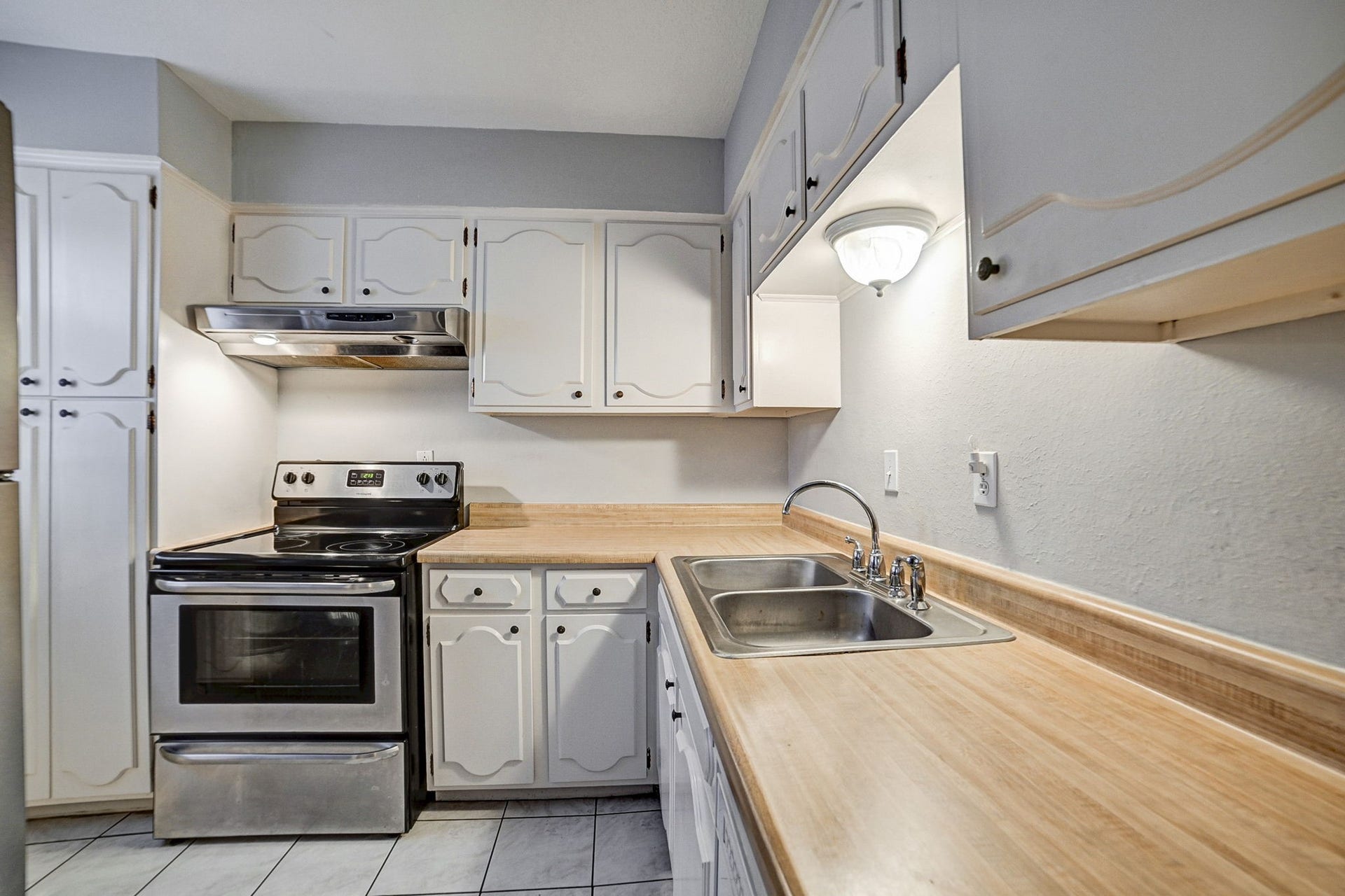 7900 Westheimer Road, #202, Houston, TX 77063 Charming kitchen featuring white cabinetry, a sleek stainless steel electric stove, and a spacious countertop with an integrated sink for convenient meal prep.