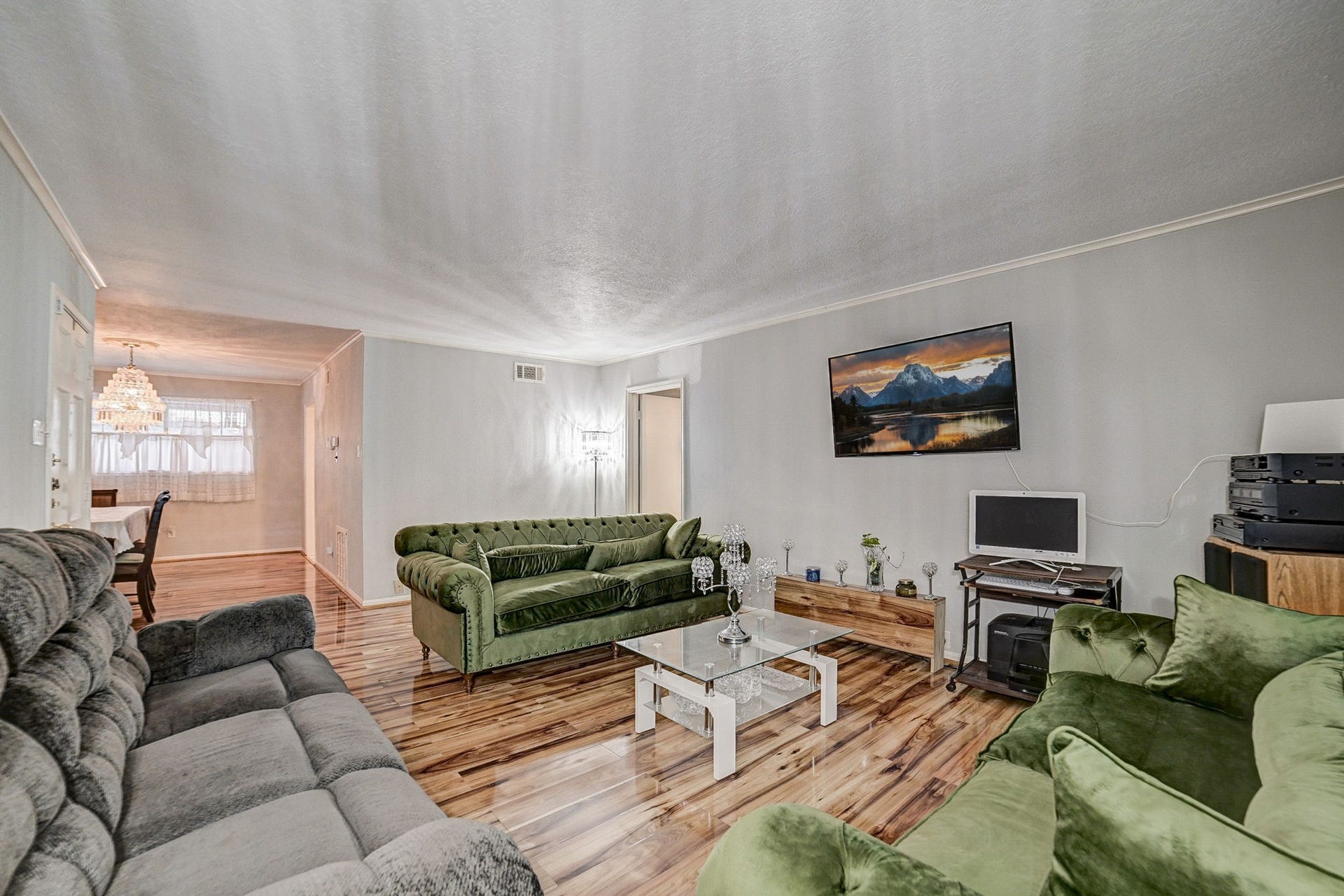 7900 Westheimer Road, #202, Houston, TX 77063 Spacious living room with elegant wood flooring, stylish green and gray sofas, and a mounted flat-screen TV, creating a cozy and inviting atmosphere.