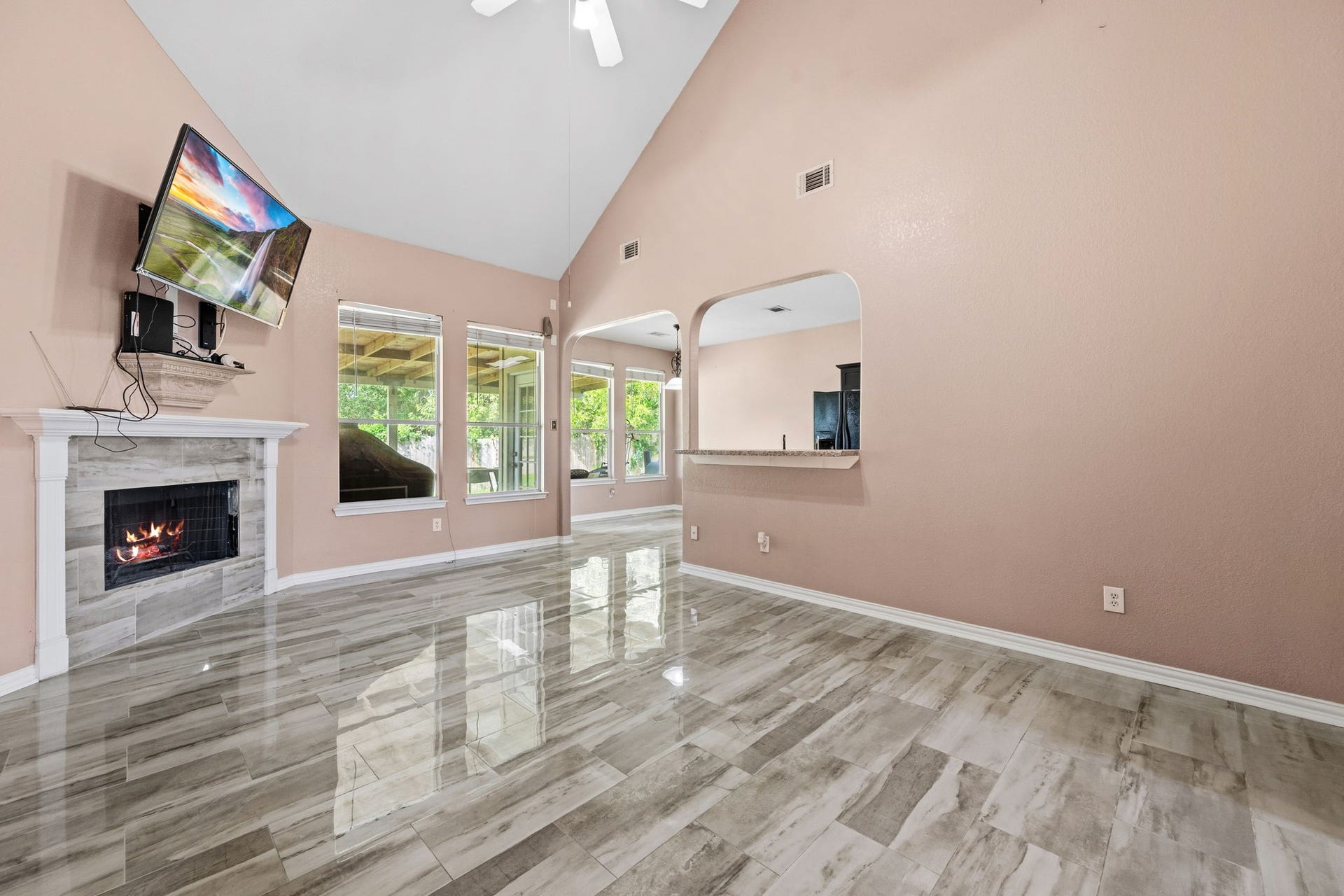 Spacious living area with high ceilings, a cozy fireplace, and large windows offering abundant natural light. The sleek tile flooring and open layout enhance the modern feel.