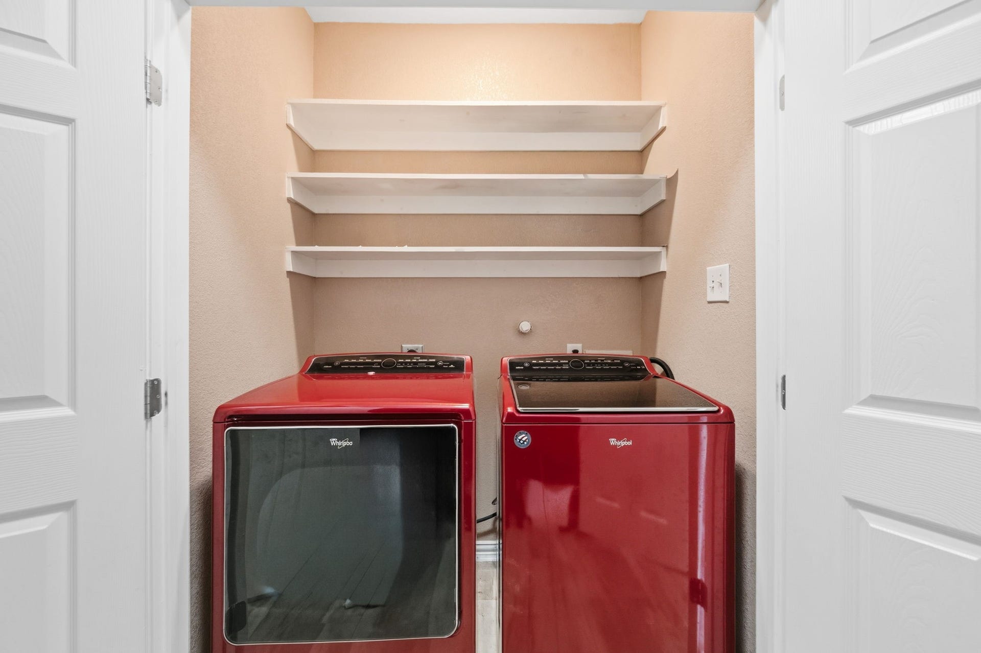 Modern laundry nook featuring sleek red washer and dryer, complemented by convenient shelving for storage.