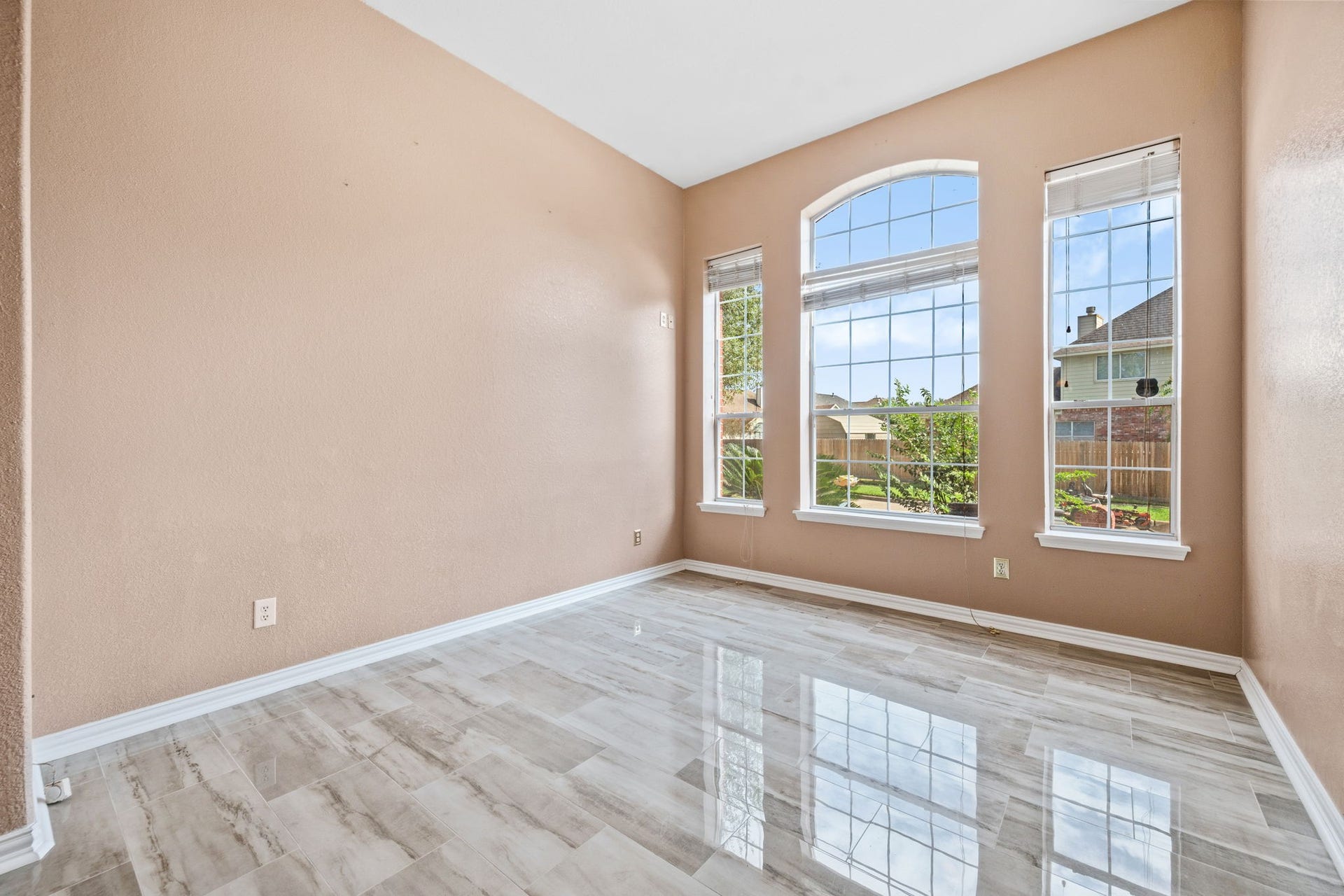 Bright and inviting room featuring large windows, elegant tiled floors, and a serene view of the lush backyard.