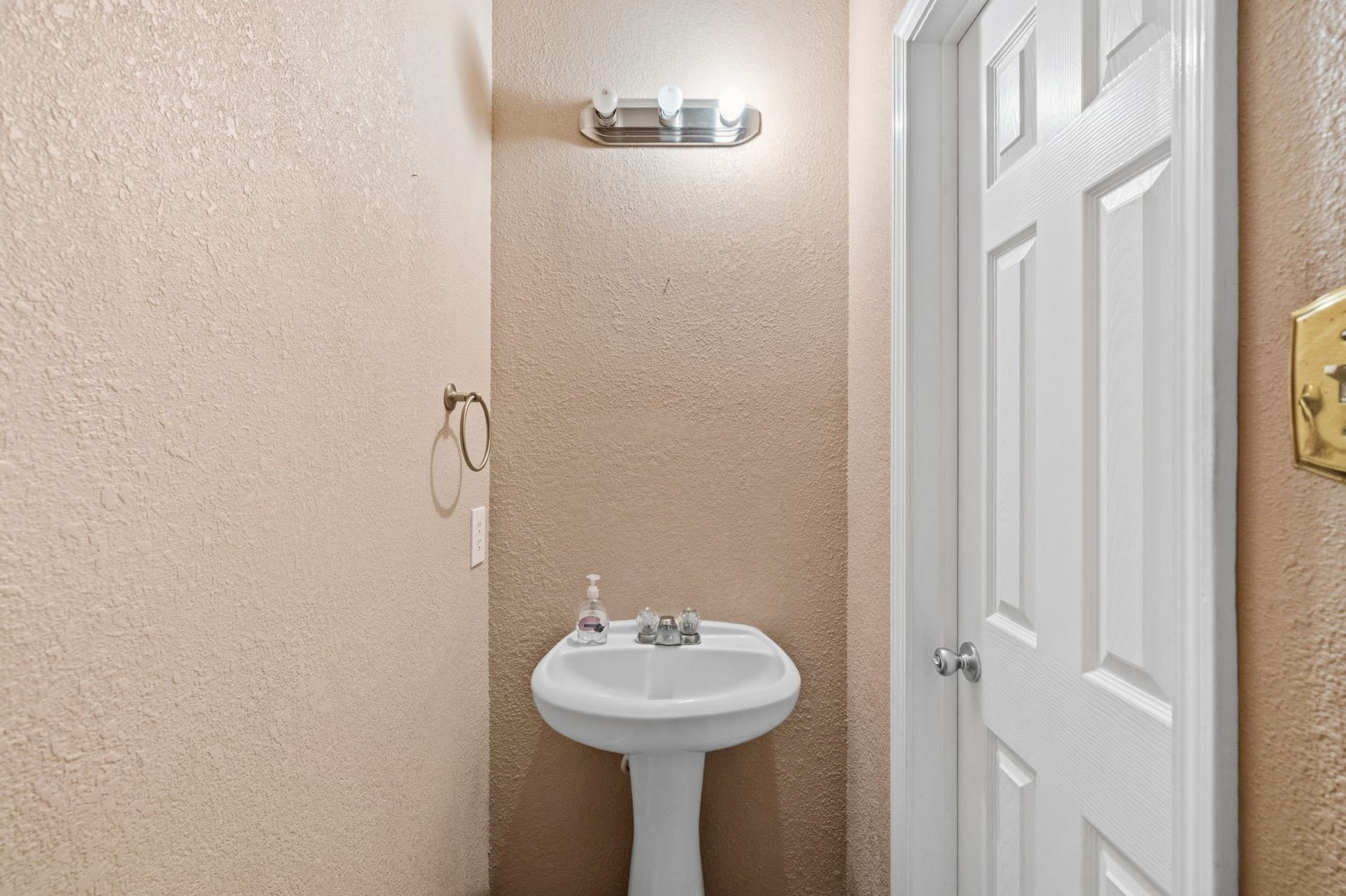 Cozy half-bathroom featuring a pedestal sink, warm-toned walls, and a modern light fixture, perfect for guests.