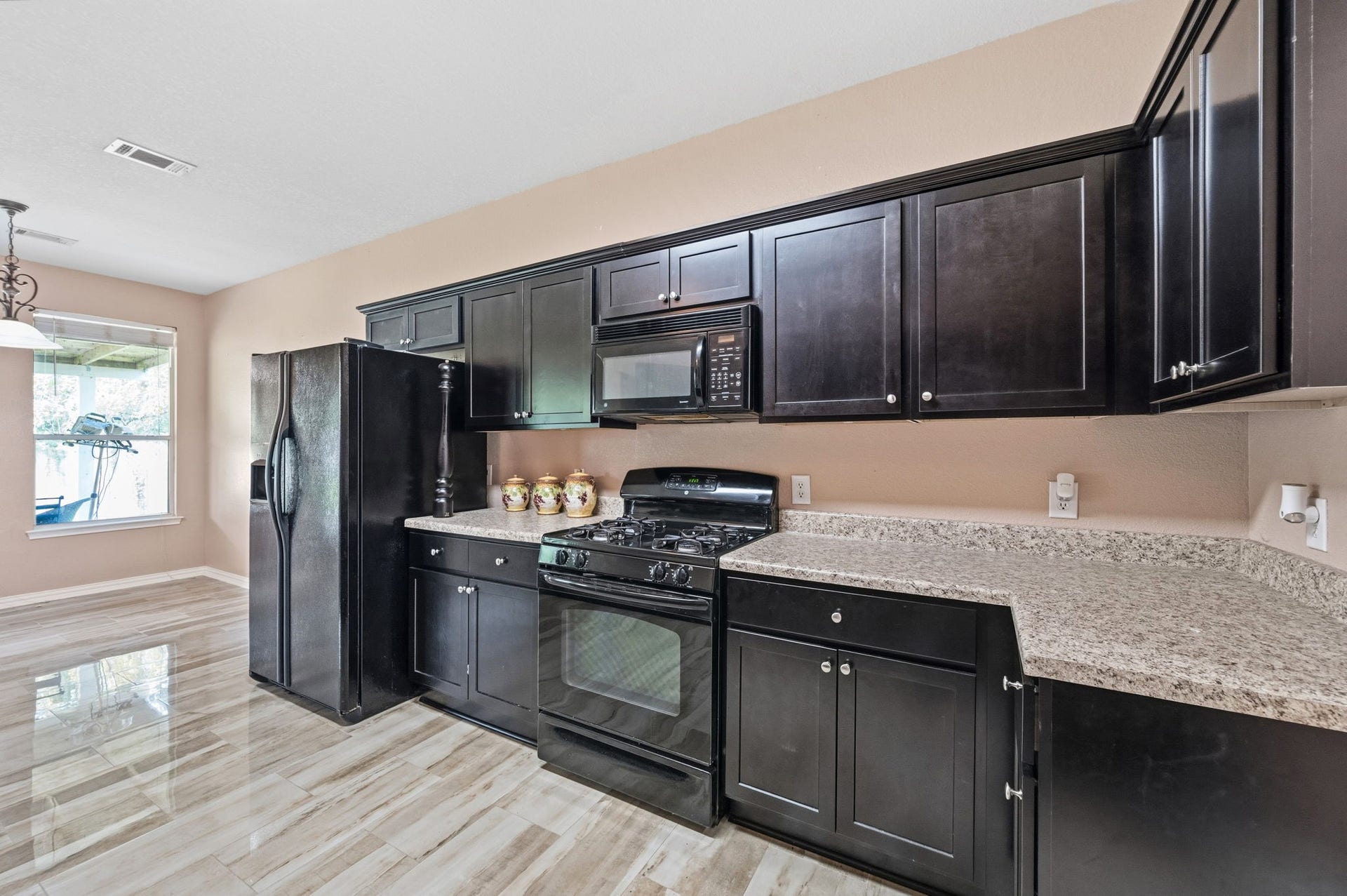 Modern kitchen featuring sleek dark cabinetry, granite countertops, and tile flooring, with ample natural light enhancing the space.