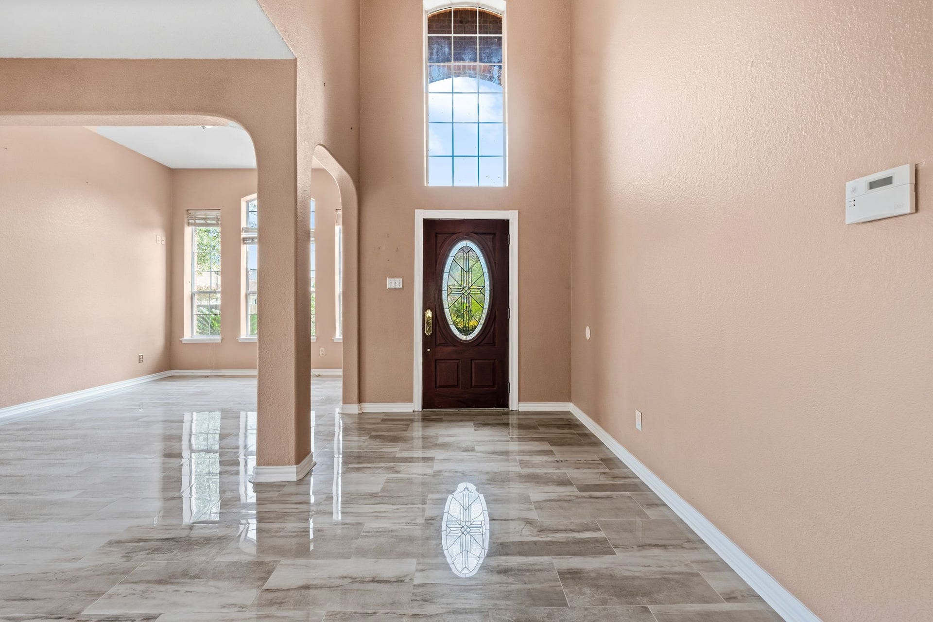 Elegant entryway featuring high ceilings, a grand arched window, and sleek tiled flooring, leading to a spacious open living area filled with natural light.