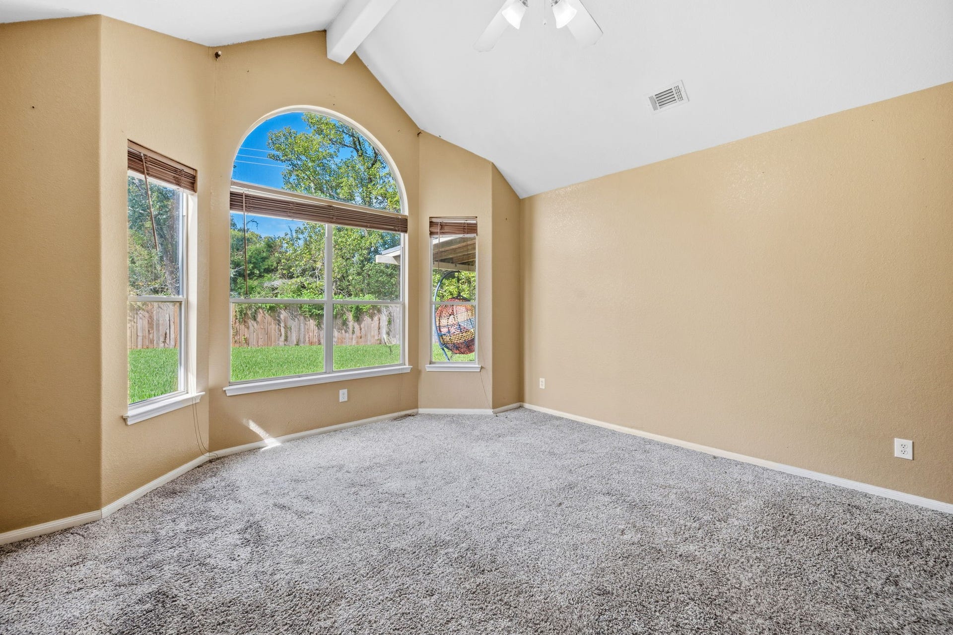 Bright and spacious room featuring vaulted ceilings and large arched windows that offer serene views of the lush backyard.