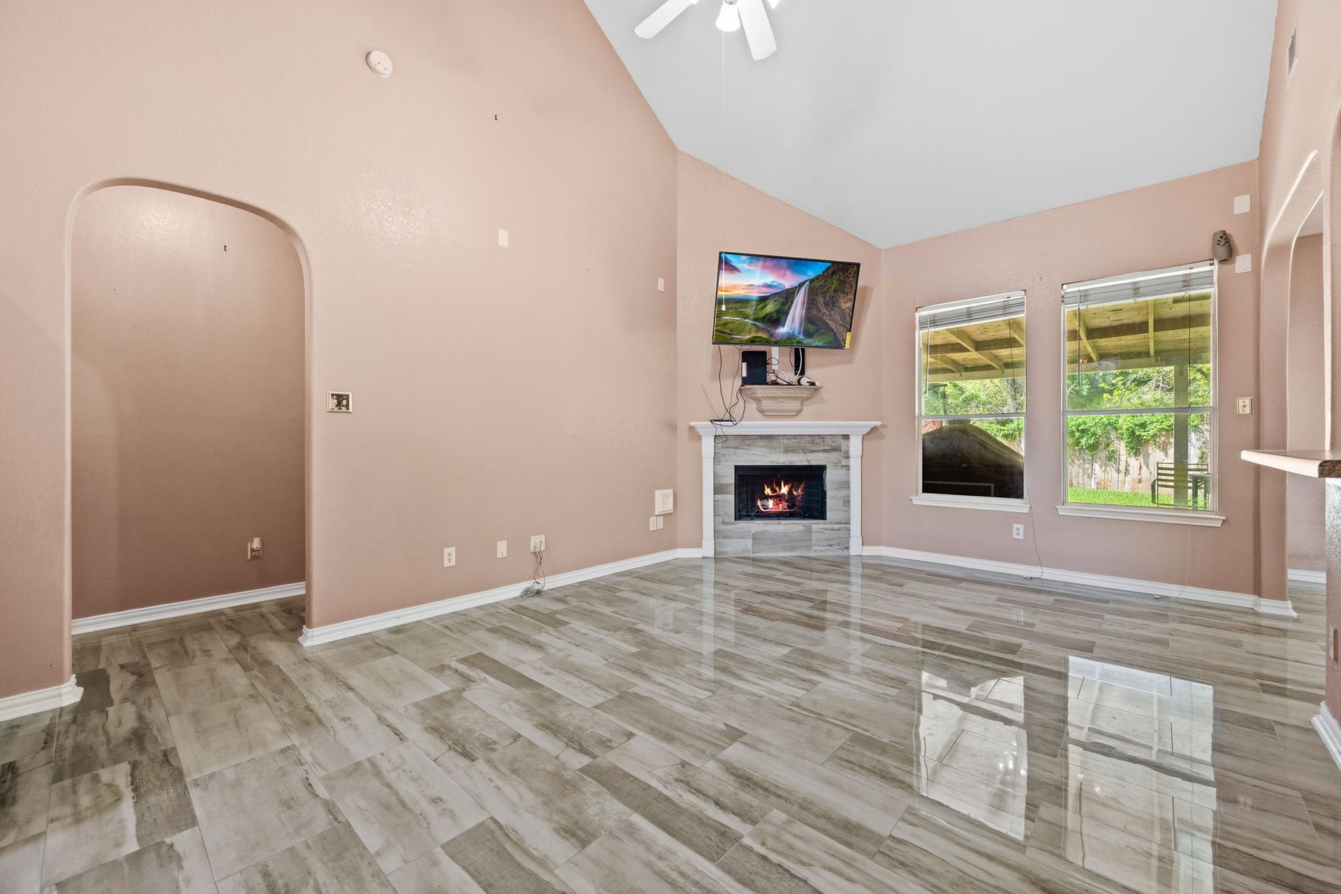 Spacious living room with high ceilings, a cozy fireplace, and large windows offering natural light and views of the lush backyard.