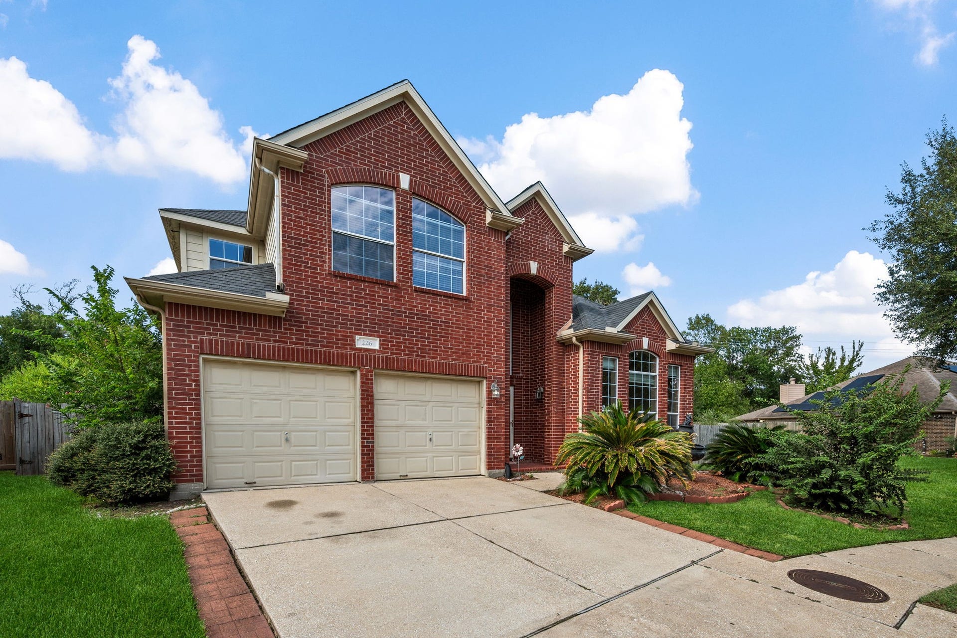 Stunning two-story brick home with a double garage, elegant arched windows, and lush landscaping on a spacious driveway.