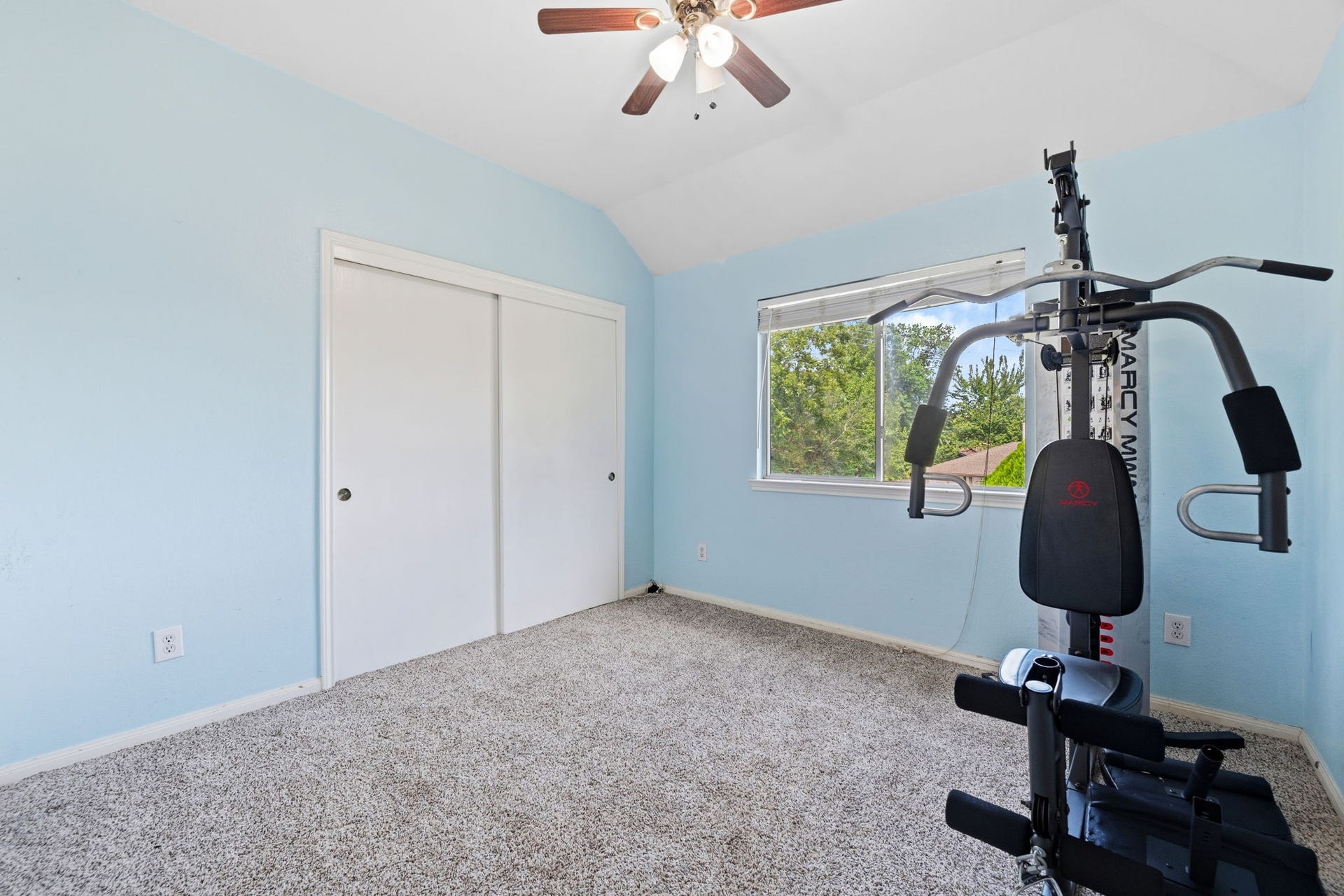 Bright and airy room featuring soft blue walls, plush carpeting, and a versatile home gym setup, perfect for workouts or relaxation.