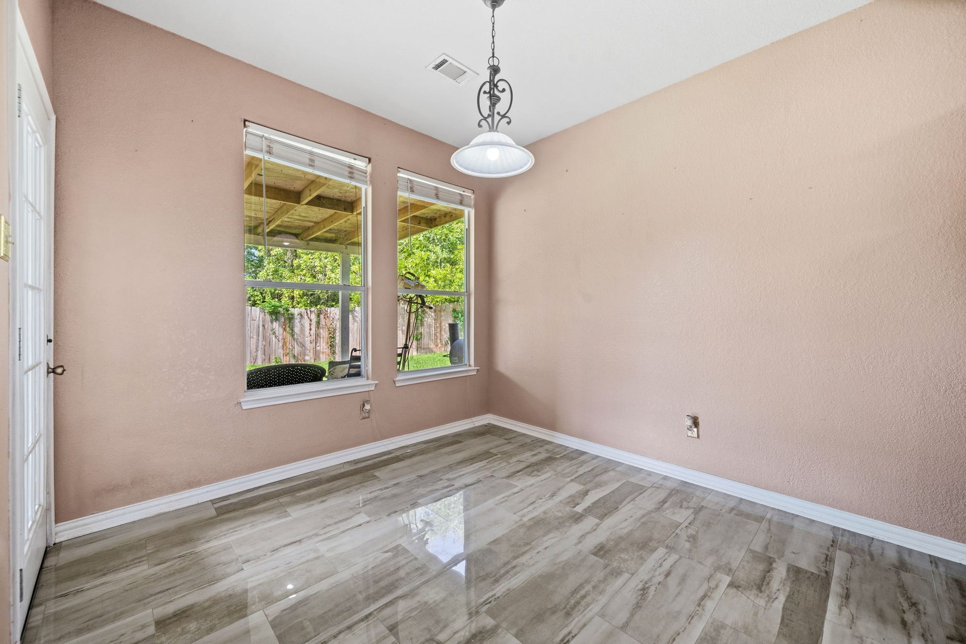 Bright and airy room featuring elegant tile flooring, large windows with views of the lush backyard, and a stylish overhead light fixture.