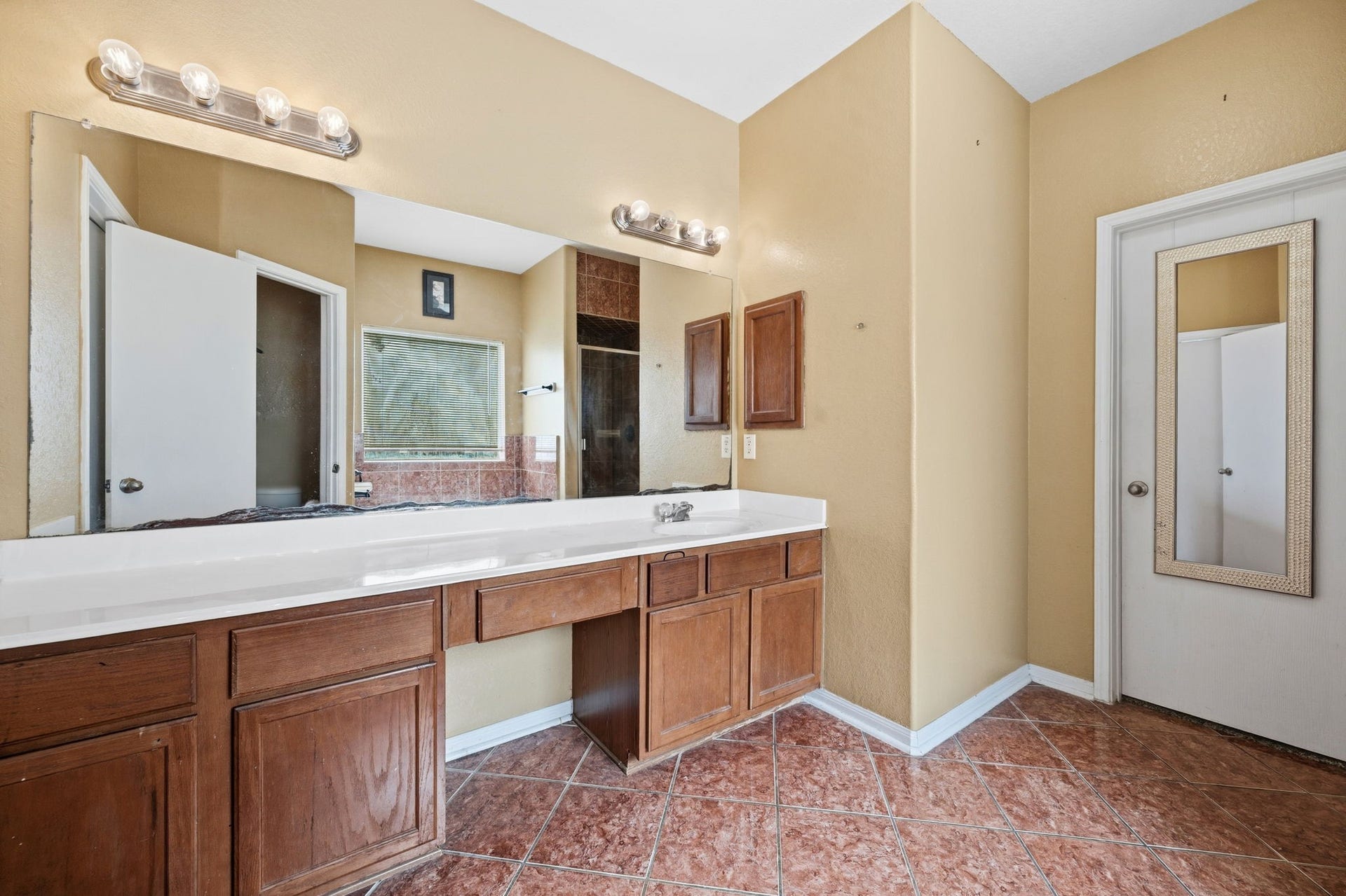Spacious bathroom featuring dual vanity sinks, warm wood cabinetry, and elegant tile flooring, complemented by ample lighting and a large mirror for a bright, inviting atmosphere.