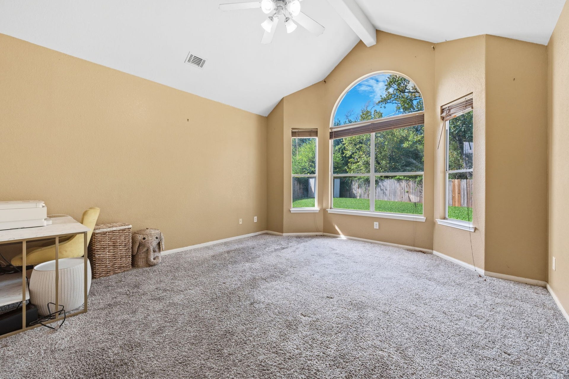 Spacious room with vaulted ceilings and large arched windows offering abundant natural light and a view of the lush backyard.