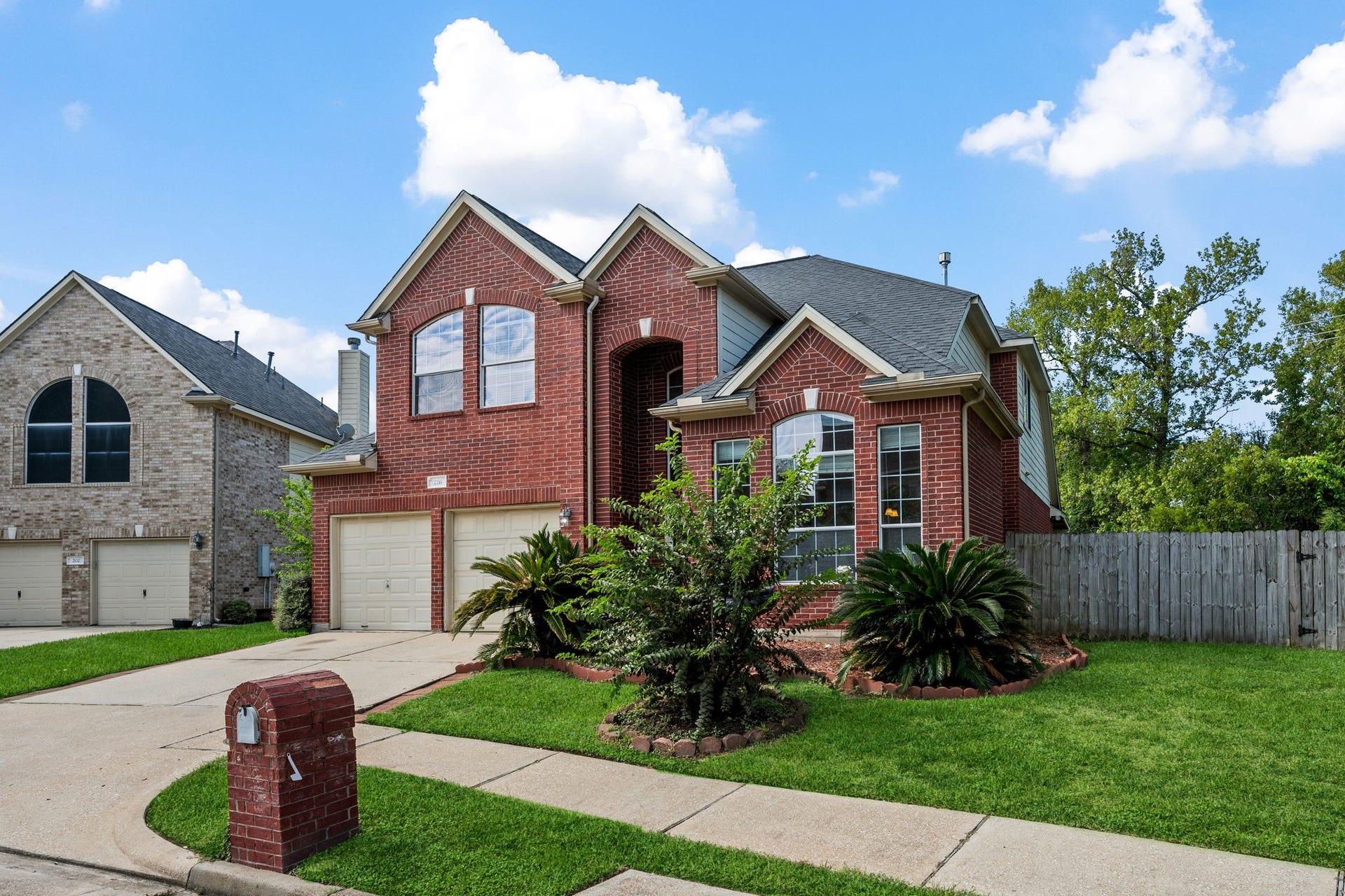Charming two-story brick home with an elegant gabled roof and a spacious two-car garage, surrounded by lush greenery and a well-maintained lawn.