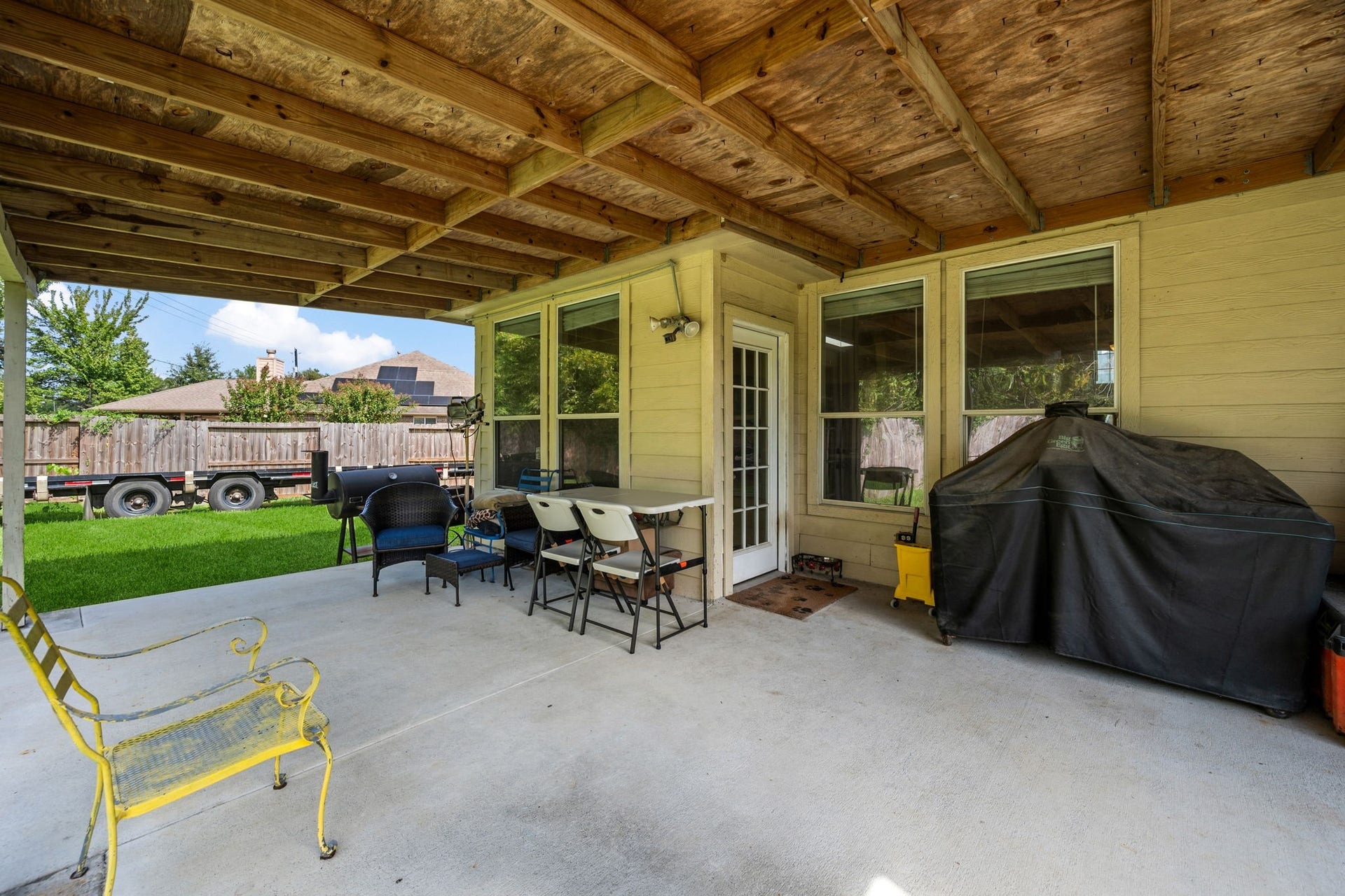 Spacious covered patio perfect for outdoor dining and entertaining, featuring ample seating, a grill, and a view of the lush backyard.