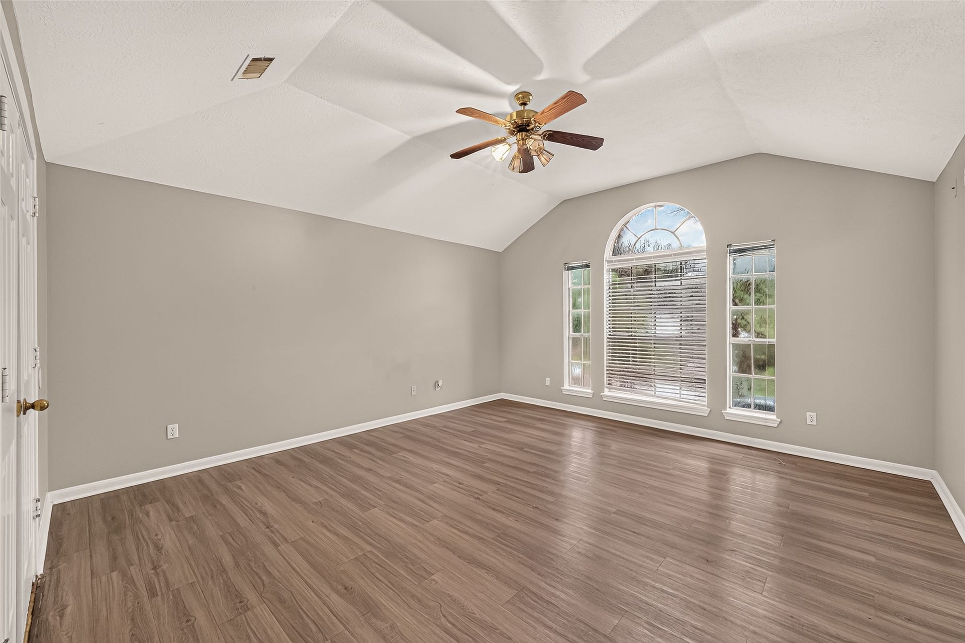 22818 Williamschase Drive, Katy, TX 77449 Impressive and spacious primary suite featuring elegant tray ceilings, beautiful vinal wood looking floors, stunning arched window flanked by two additional windows, filling the room with natural light.