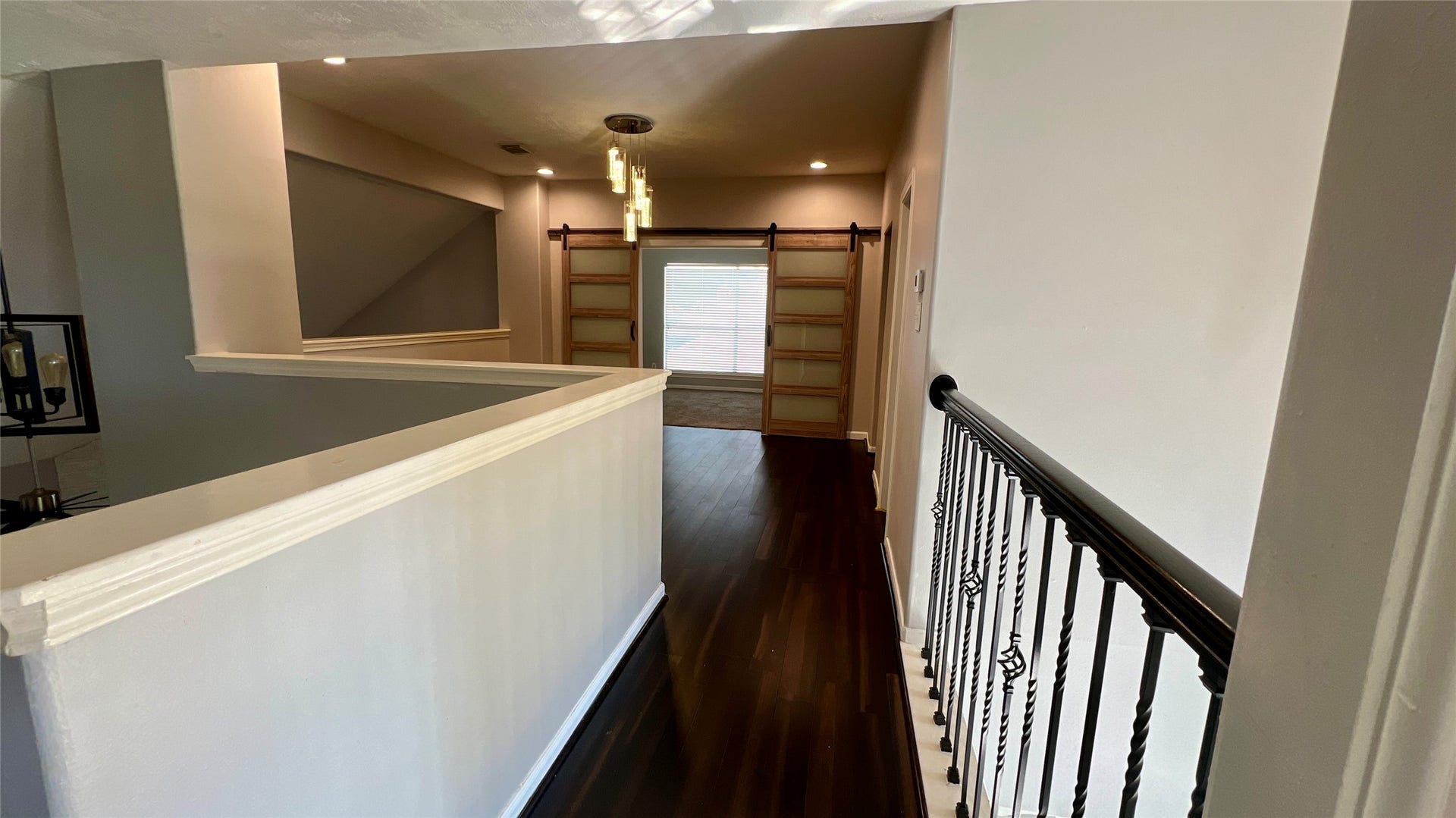 Modern upstairs hallway w/ sliding door at the end, leading to study/office with natural light. The space is bright and contemporary, with recessed lighting.